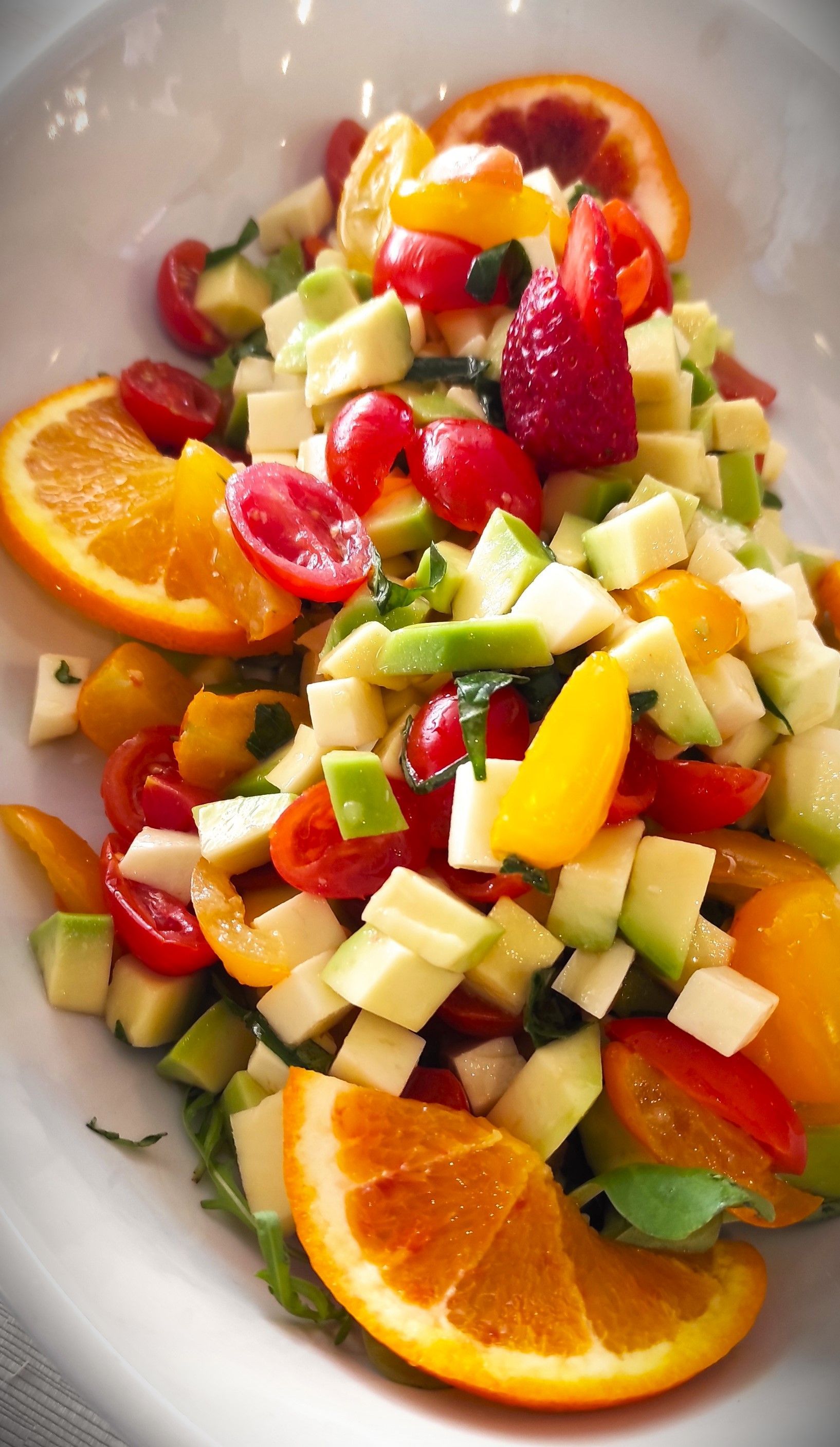 Un'insalata con pomodori, avocado e fette d'arancia su un piatto bianco