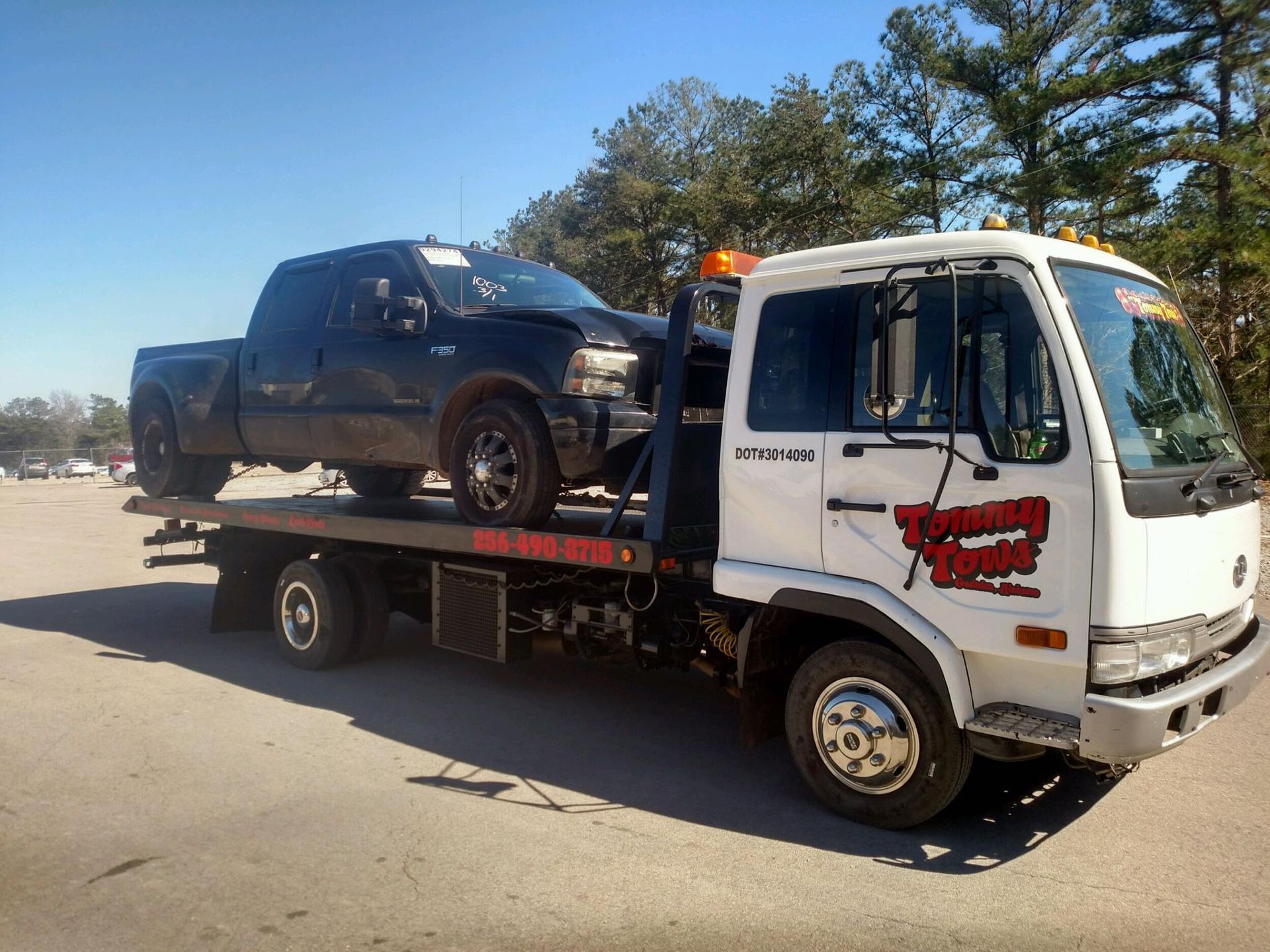 Tow truck carrying a black pickup truck on a sunny day.