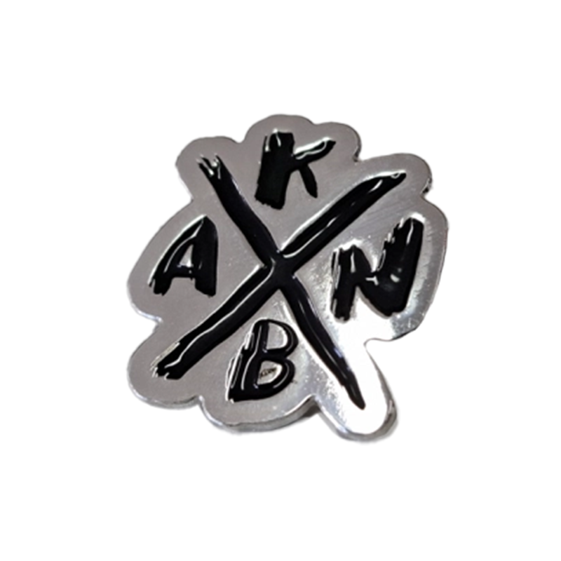 Silberne Anstecknadel mit einem schwarzen X in der Mitte und den Buchstaben A, K, B, N.