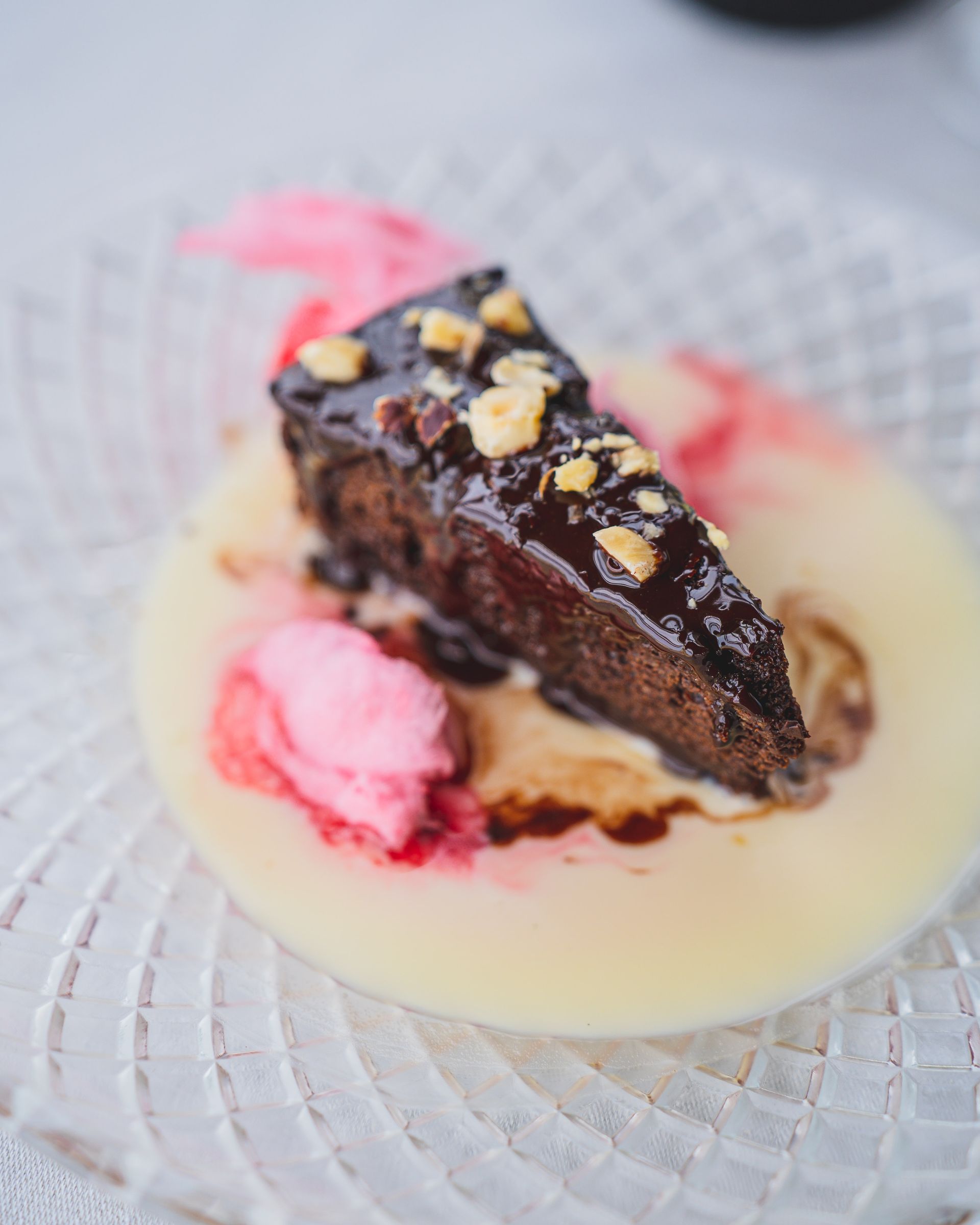 Rebanada de pastel de chocolate con glaseado y nueces, servida en un plato con salsa de vainilla y salsa rosa.