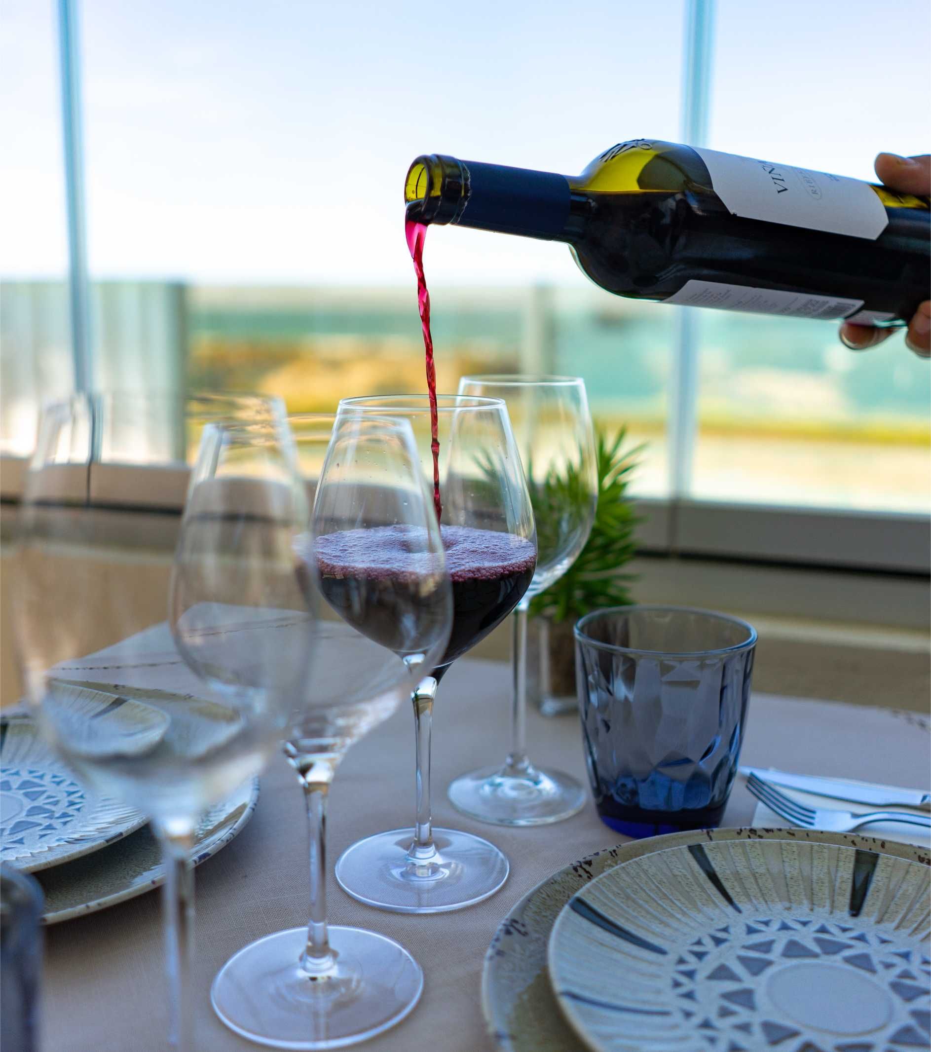 Vino tinto vertido en una copa en una mesa preparada con platos, otras copas y un vaso azul.