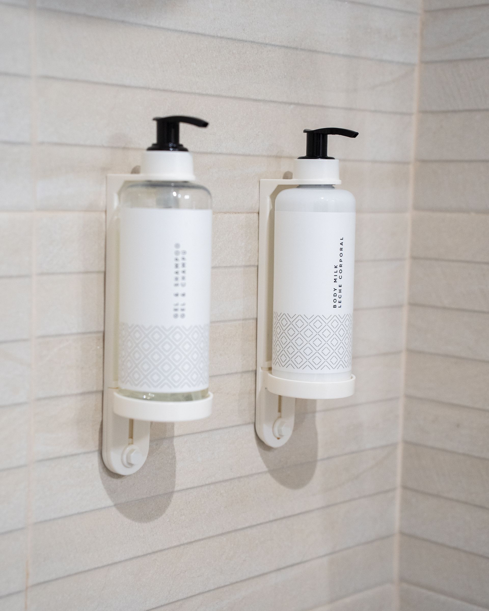 Dos botellas blancas y negras montadas en una pared de azulejos, probablemente dispensadores de champú y acondicionador.