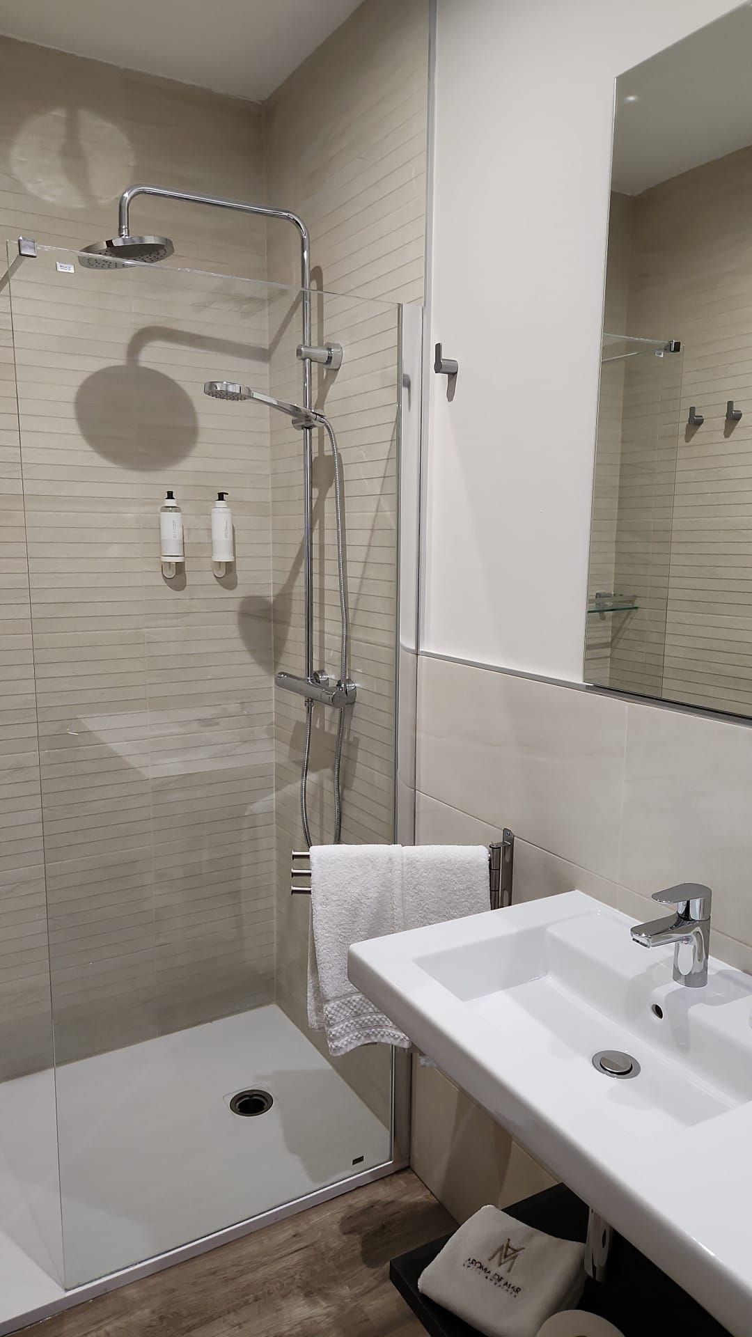 Baño con ducha y lavabo. La ducha tiene mampara de cristal, azulejos neutros y grifería plateada. Lavabo blanco.