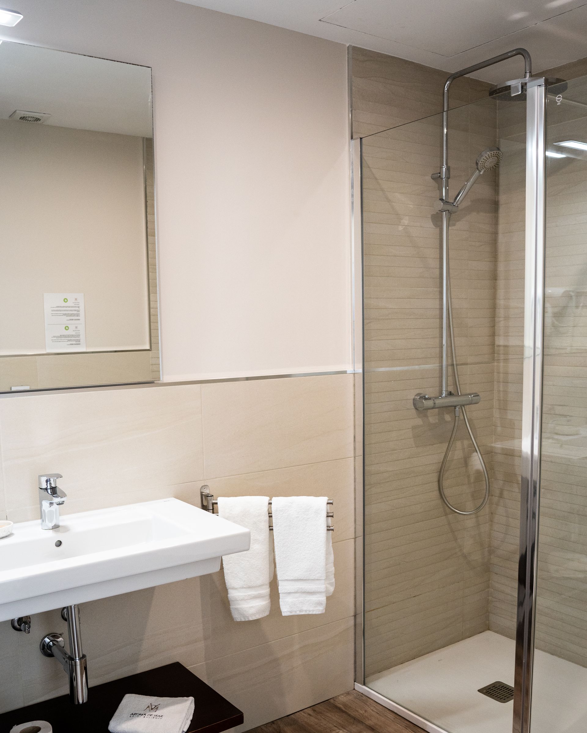 Baño con lavabo, espejo, ducha y toallas; tonos neutros.