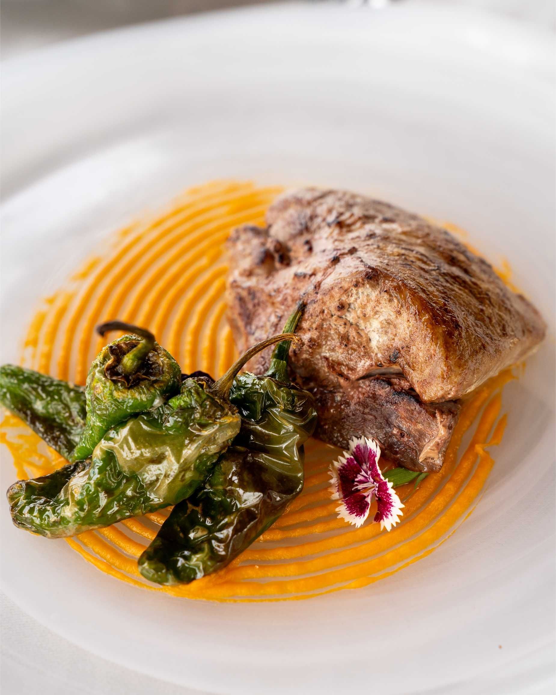 Carne a la parrilla con pimientos verdes y puré de naranja en un plato blanco.