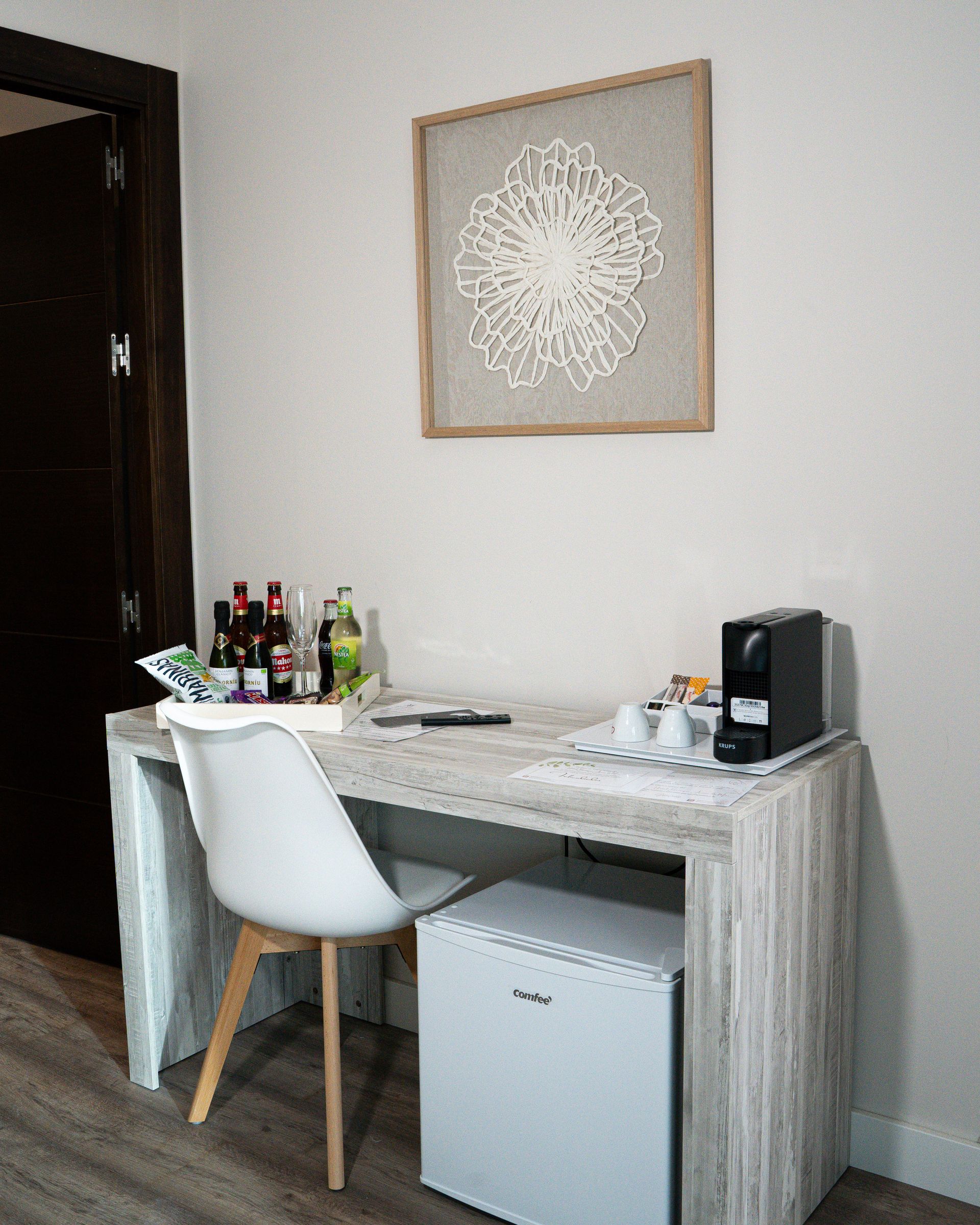 Escritorio con silla blanca y mininevera. Sobre el escritorio, una pieza decorativa de pared.