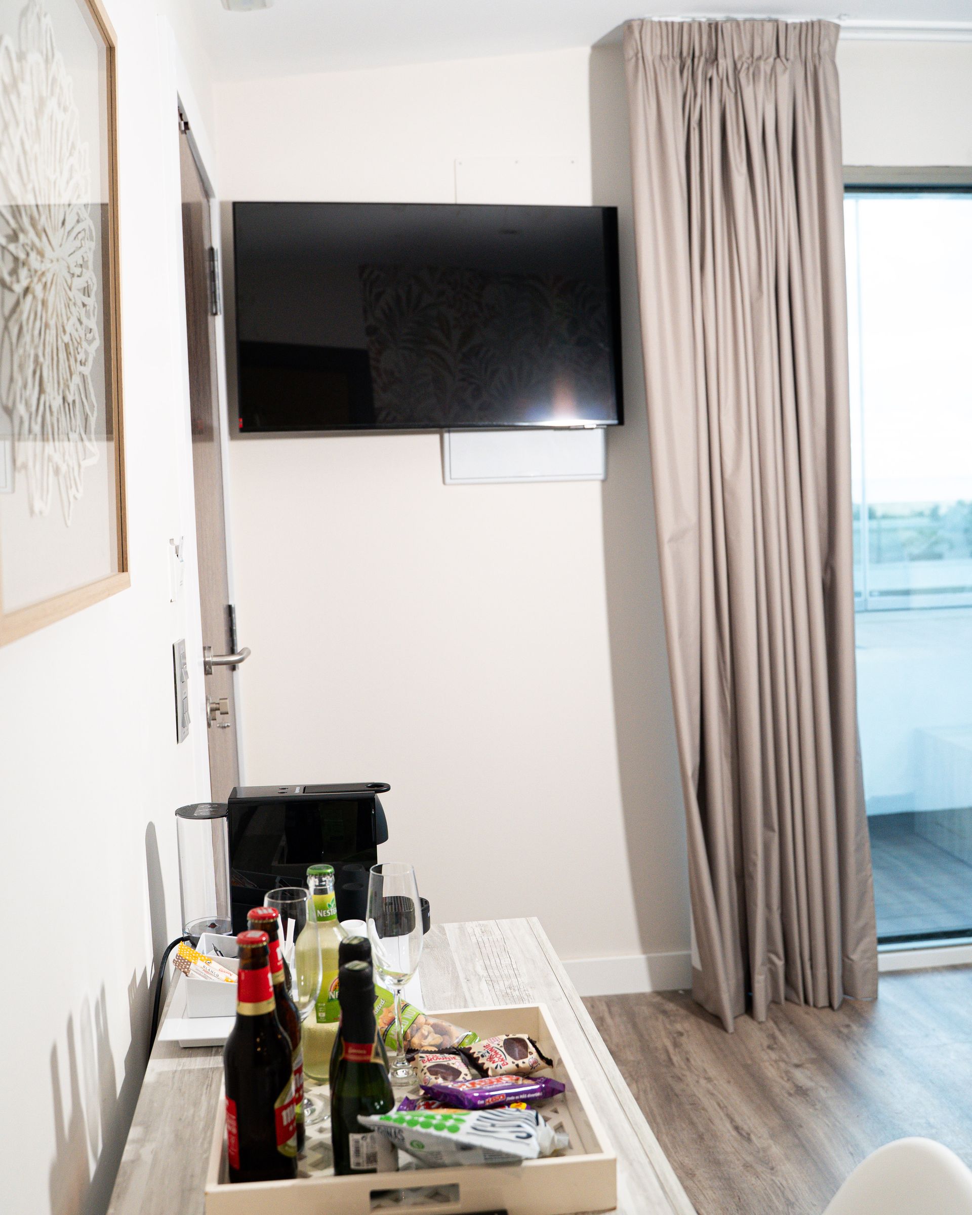 Una habitación con un televisor en la pared, una bandeja de bocadillos y una ventana con cortinas.