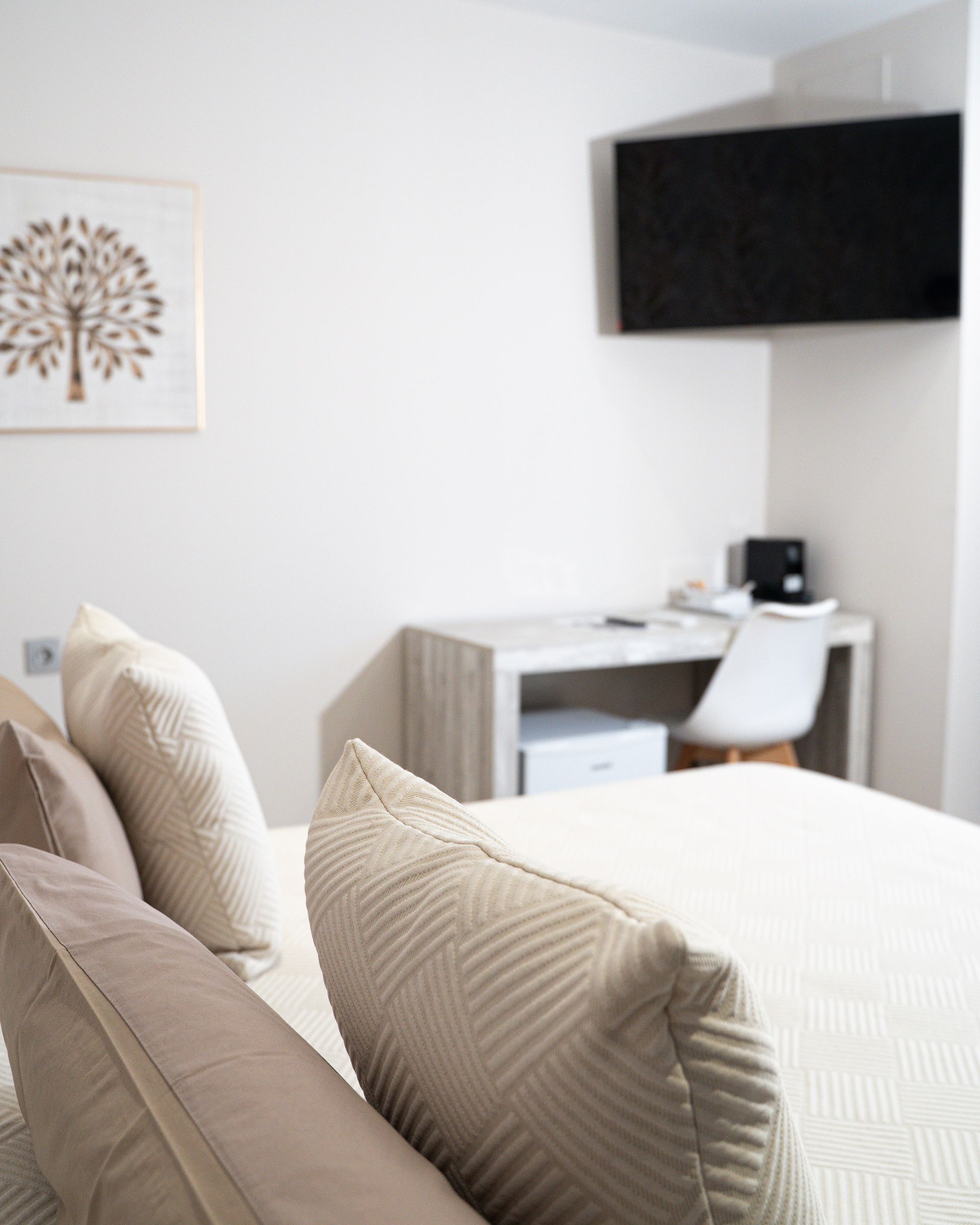 Cama con almohadas, escritorio y televisión en habitación luminosa.