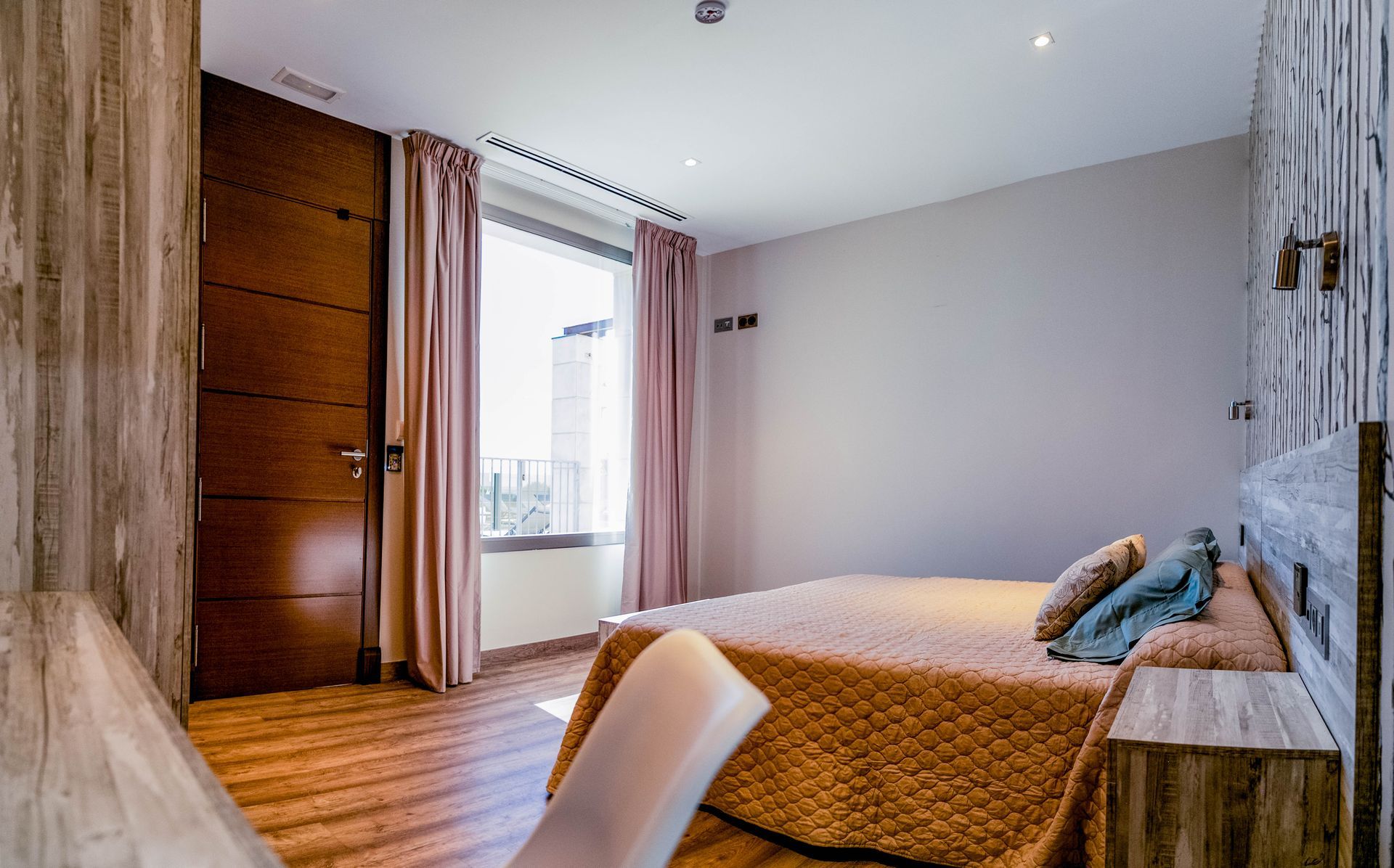 Dormitorio con cama, ventana con cortinas, revestimiento de madera y puerta cerrada.