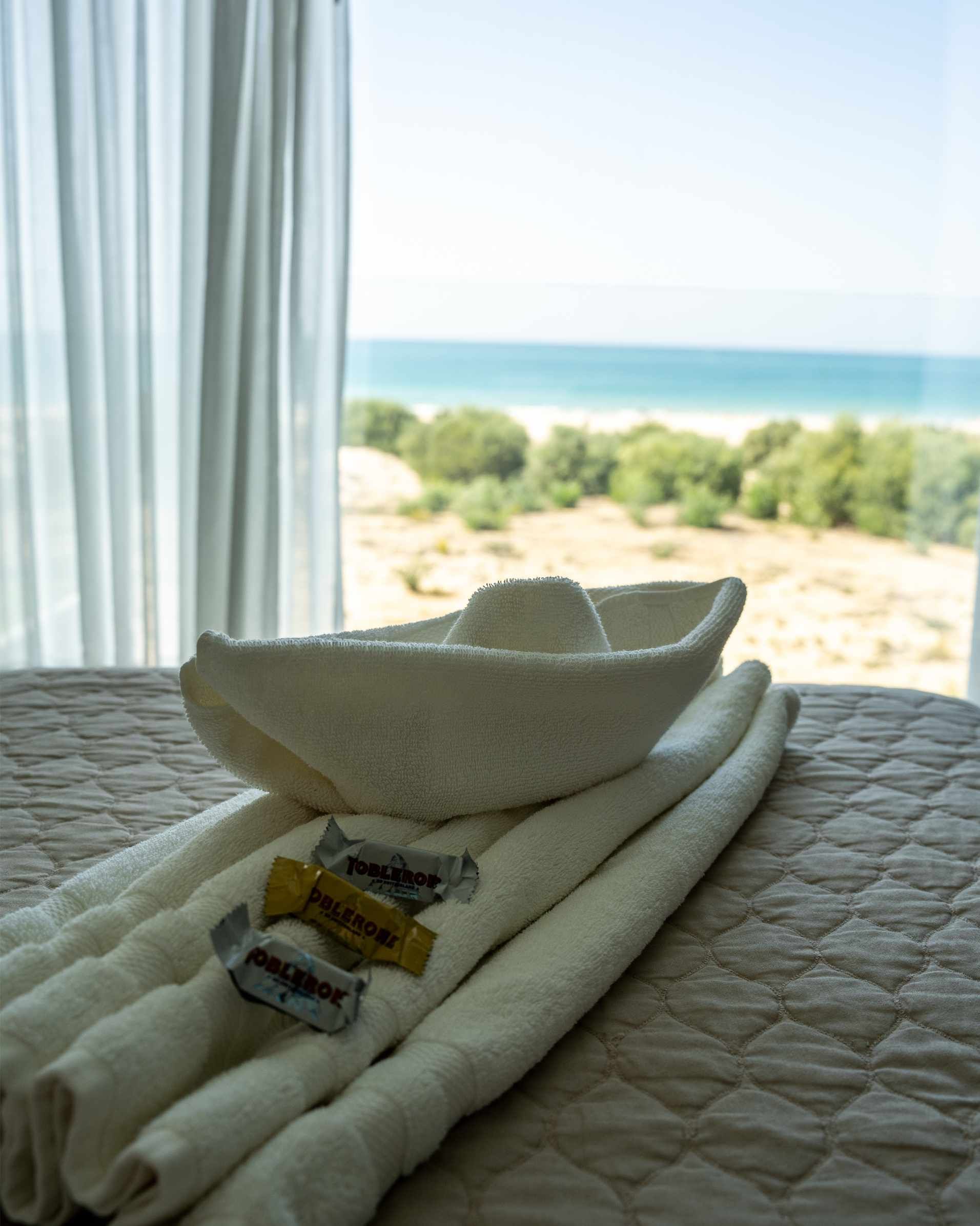 Barco de toalla blanca con dulces sobre la cama, vista al mar a través de la ventana.