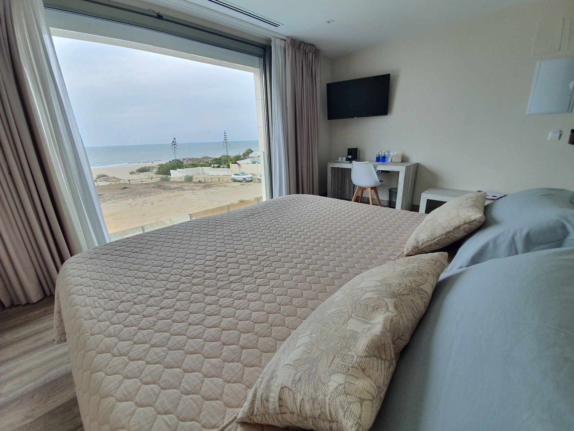 Dormitorio con cama, gran ventanal con vistas a la playa, escritorio y TV montada.