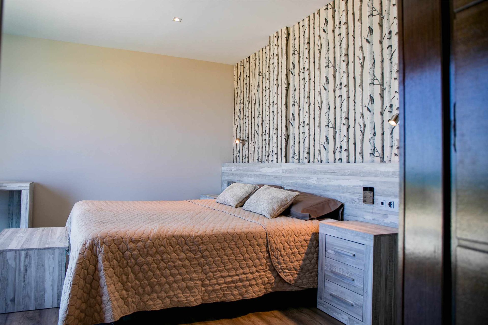 Dormitorio con cama, papel tapiz de abedul y detalles de madera.