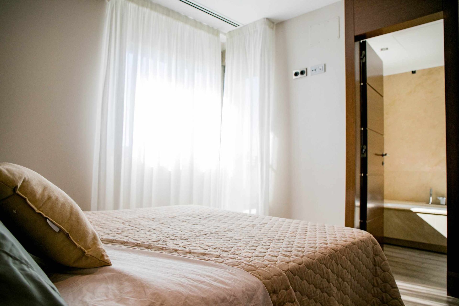Dormitorio con cama, cortinas transparentes y puerta abierta a un baño.