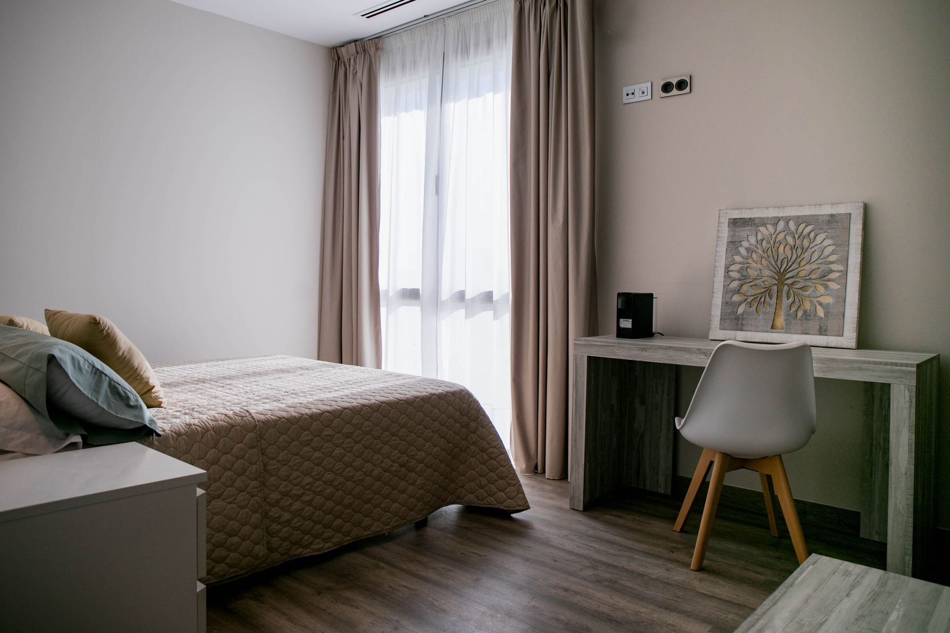 Dormitorio con cama, escritorio, silla, ventana con cortinas y arte de pared.