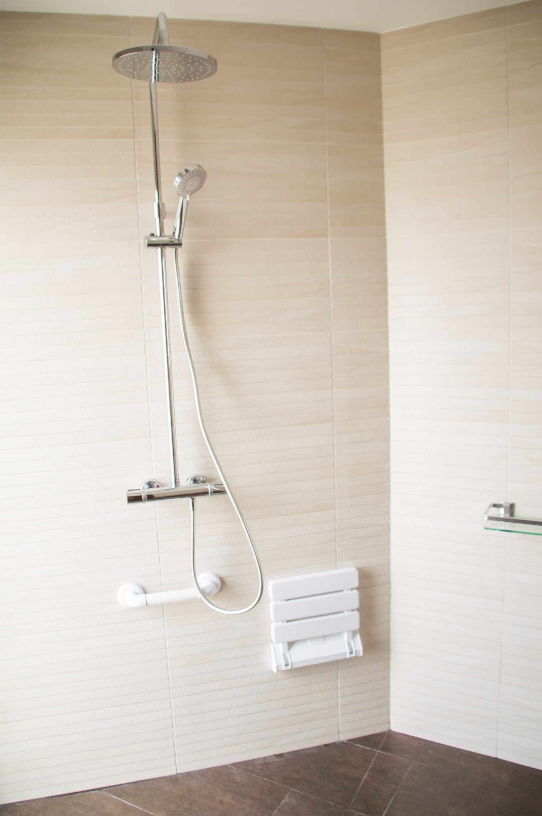 Ducha con cabezal de lluvia, ducha de mano y asiento abatible sobre pared de azulejos. Incluye barra de apoyo y toallero.