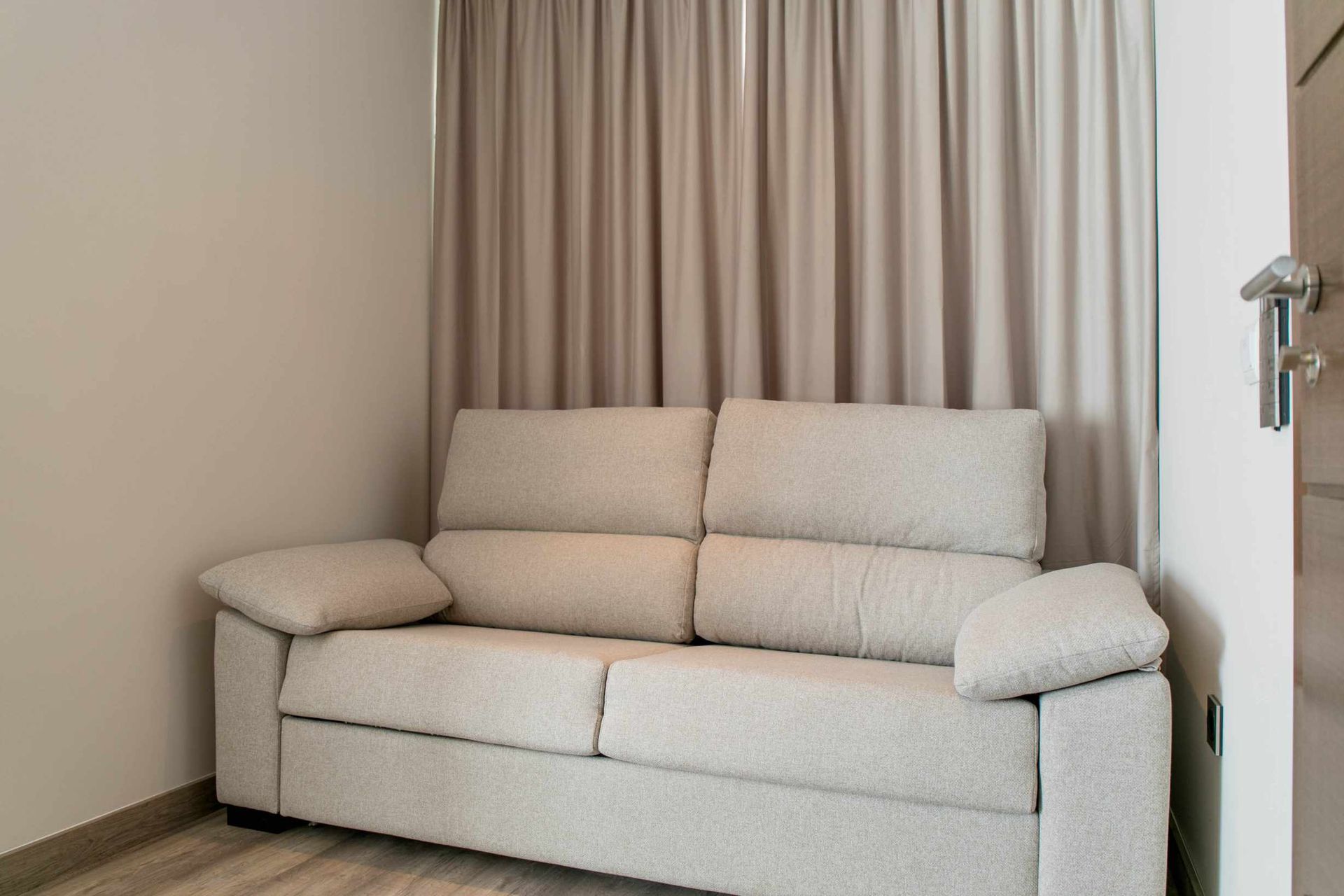 Sofá de color claro contra una cortina beige en una habitación con paredes claras.
