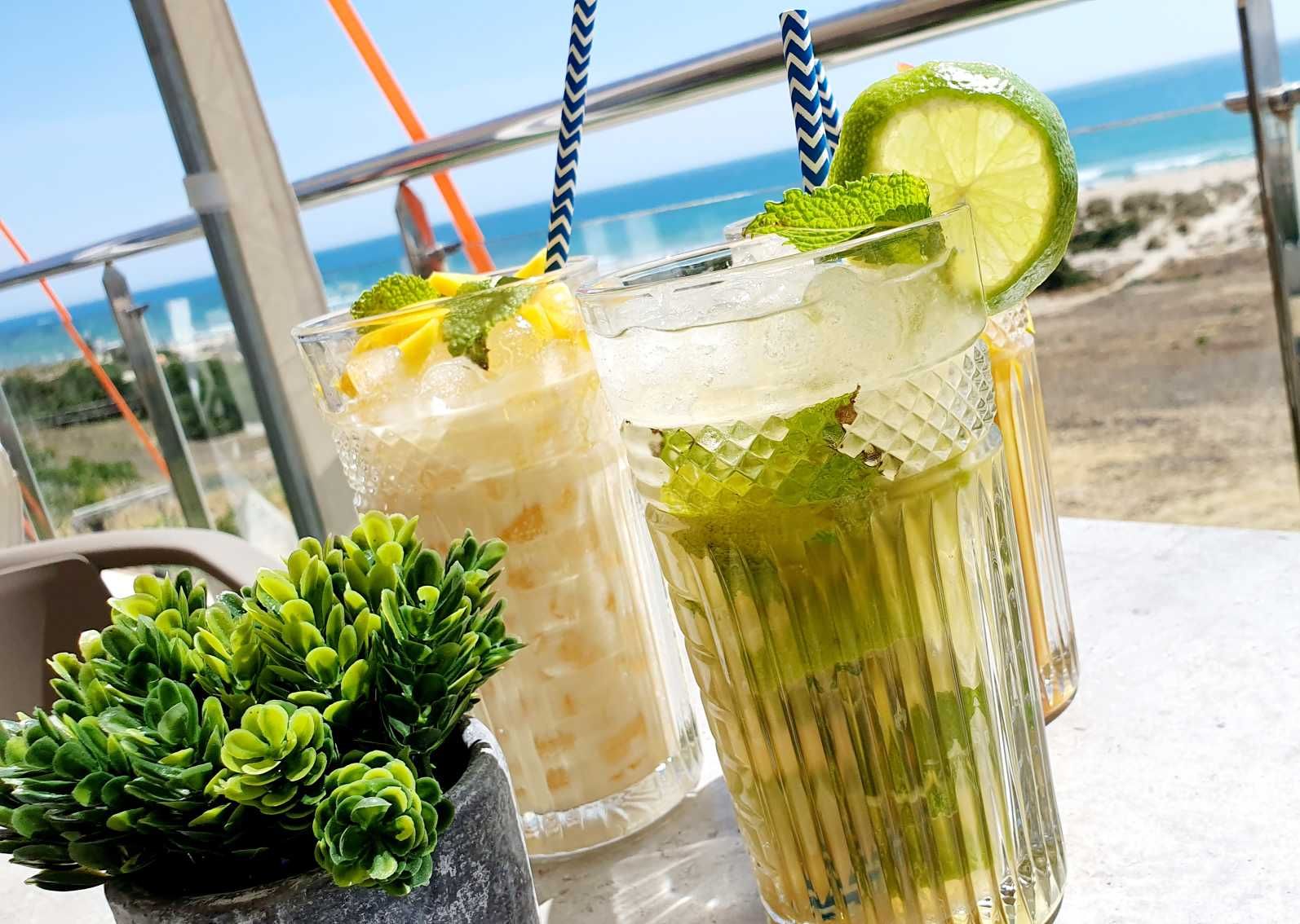 Tres cócteles con menta y cítricos en una mesa, con vistas al mar.