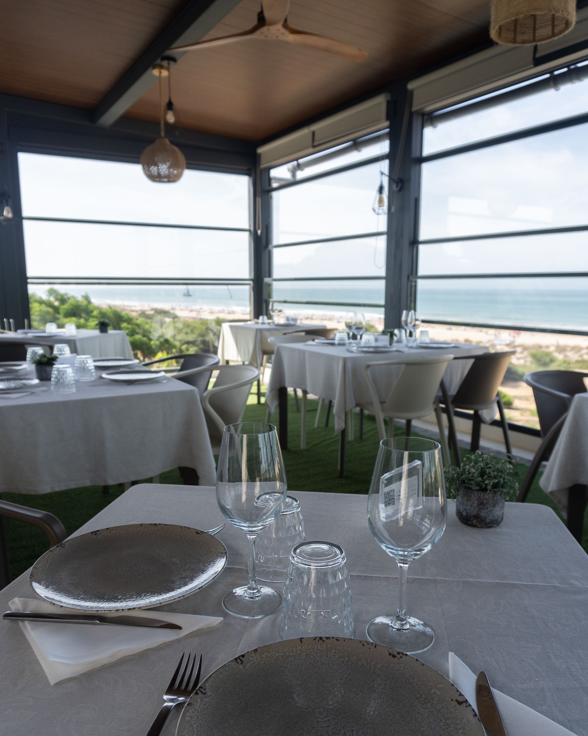 Restaurante con mesas dispuestas para cenar, con vista a la playa y al mar.