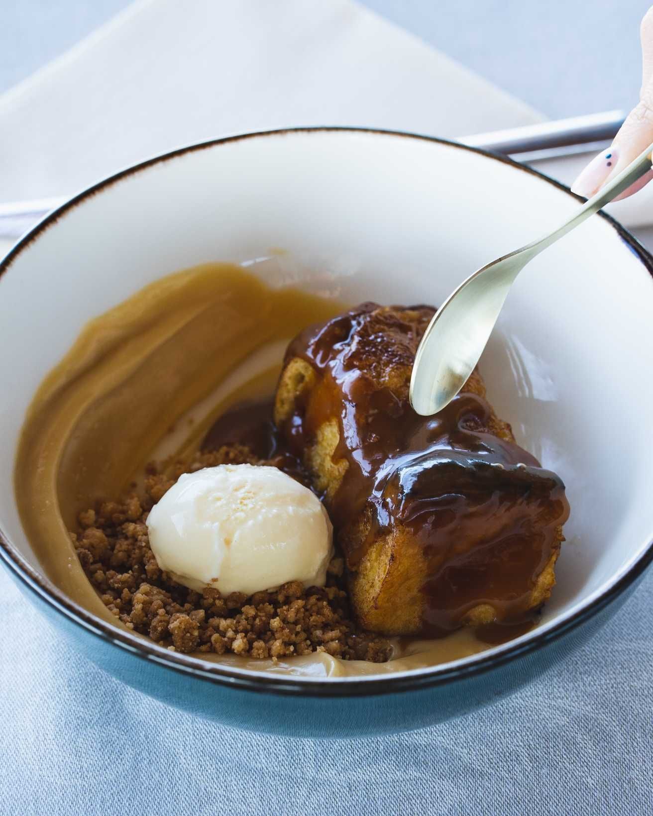 Cuenco de postre con bizcocho, helado, salsa y cuchara.