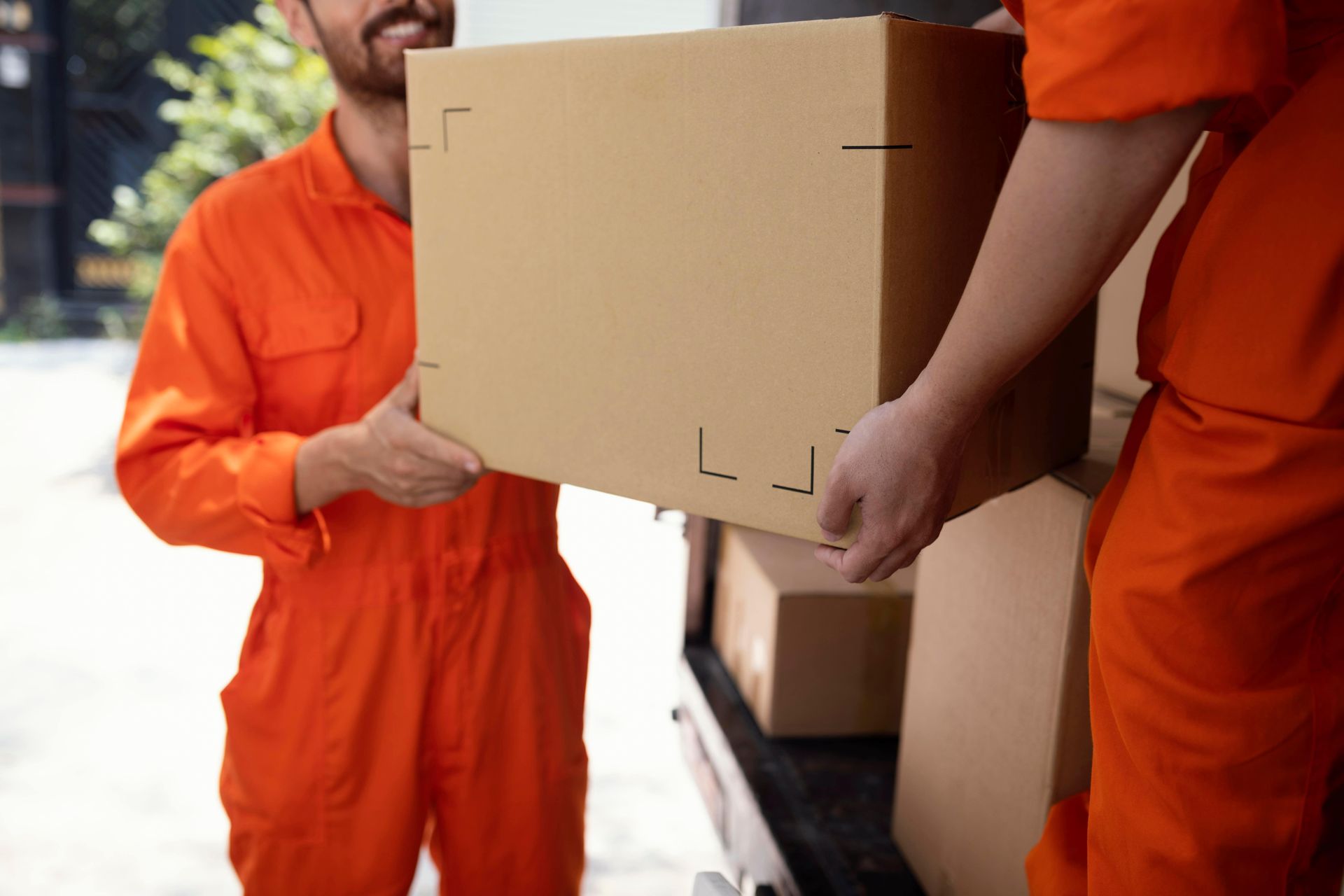 Two people in orange jumpsuits loading a cardboard box into a vehicle.