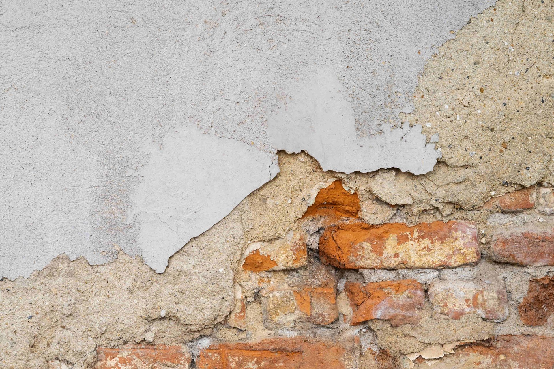 Exposed brick wall with peeling, textured plaster in shades of white, beige, and orange.