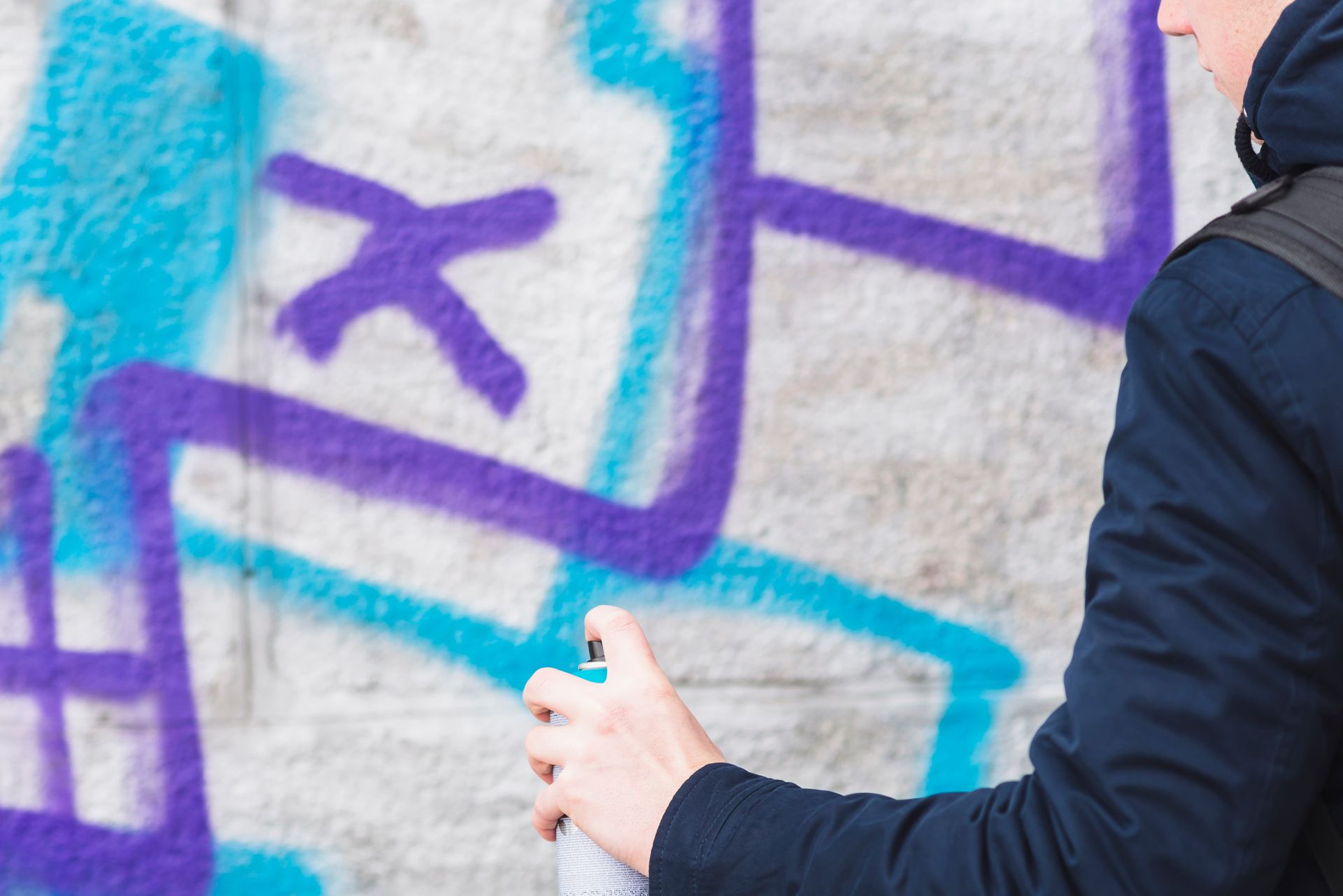 Person spraying purple graffiti on a light-colored wall, with turquoise accents.