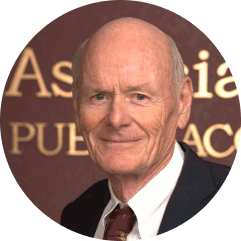 Bald man in a suit smiles at the camera, background with gold lettering on a brown surface.