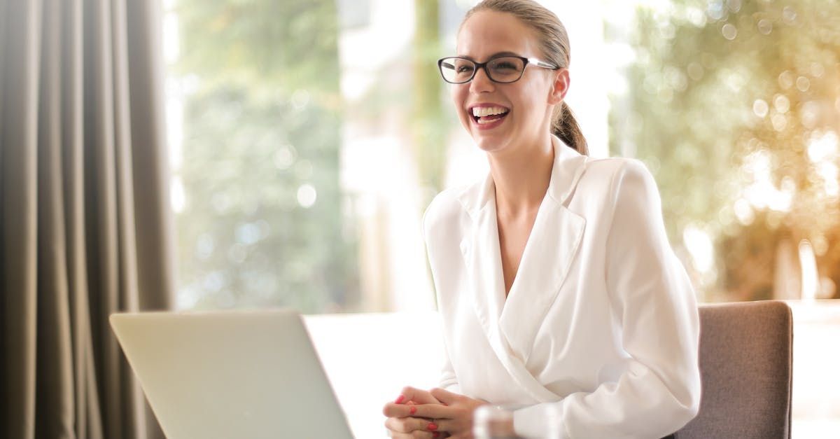 A woman is sitting at a table with a laptop and smiling.