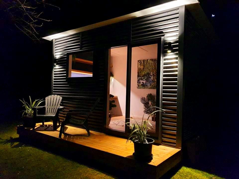 A small house with a deck and chairs in front of it at night.