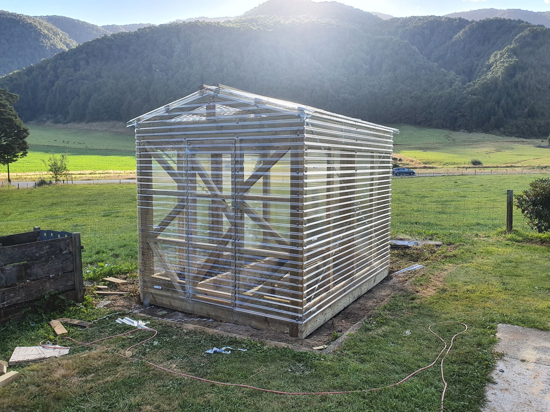 A greenhouse is being built in a grassy field with mountains in the background.