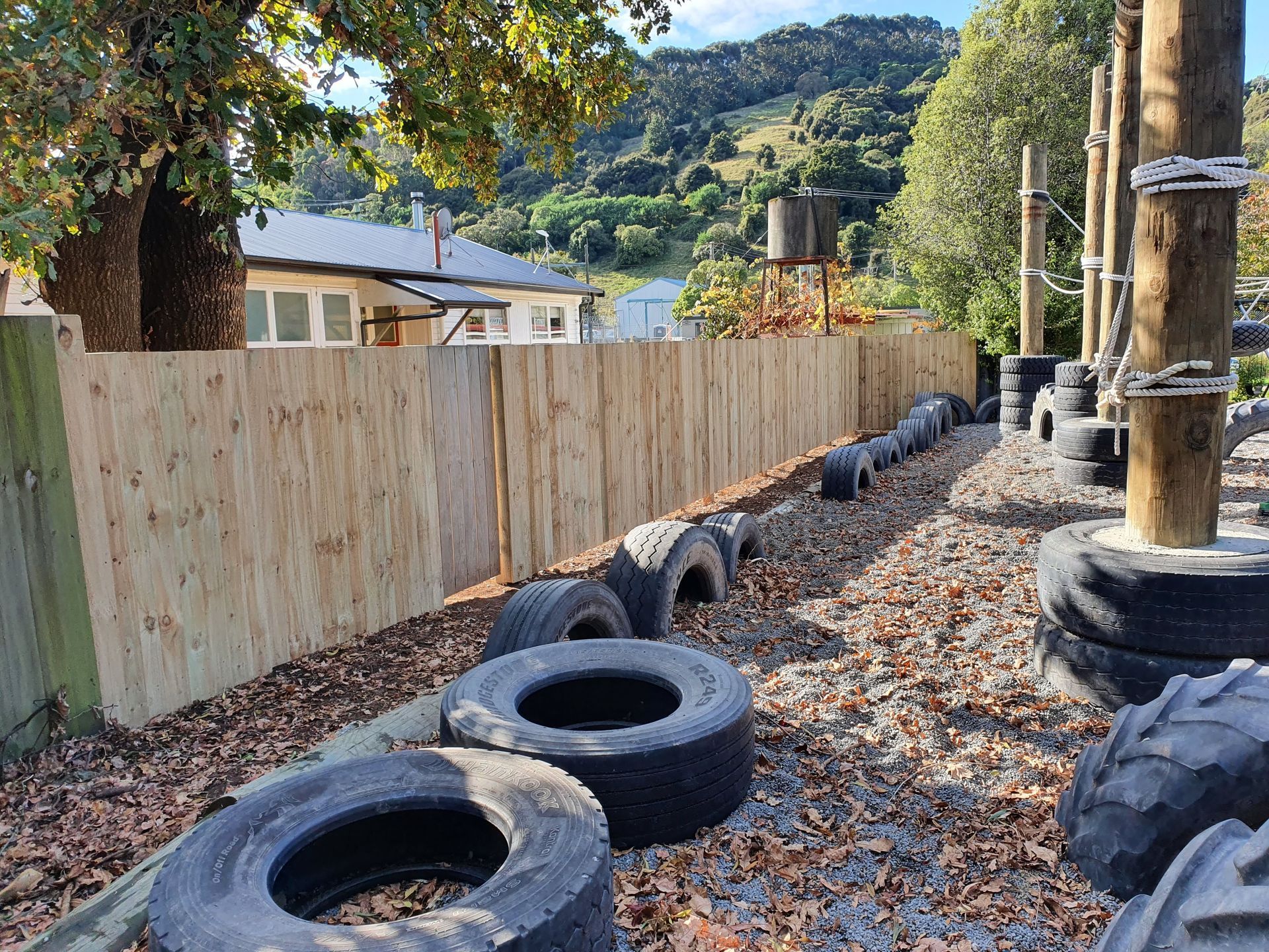 A bunch of tires are sitting next to a wooden fence.