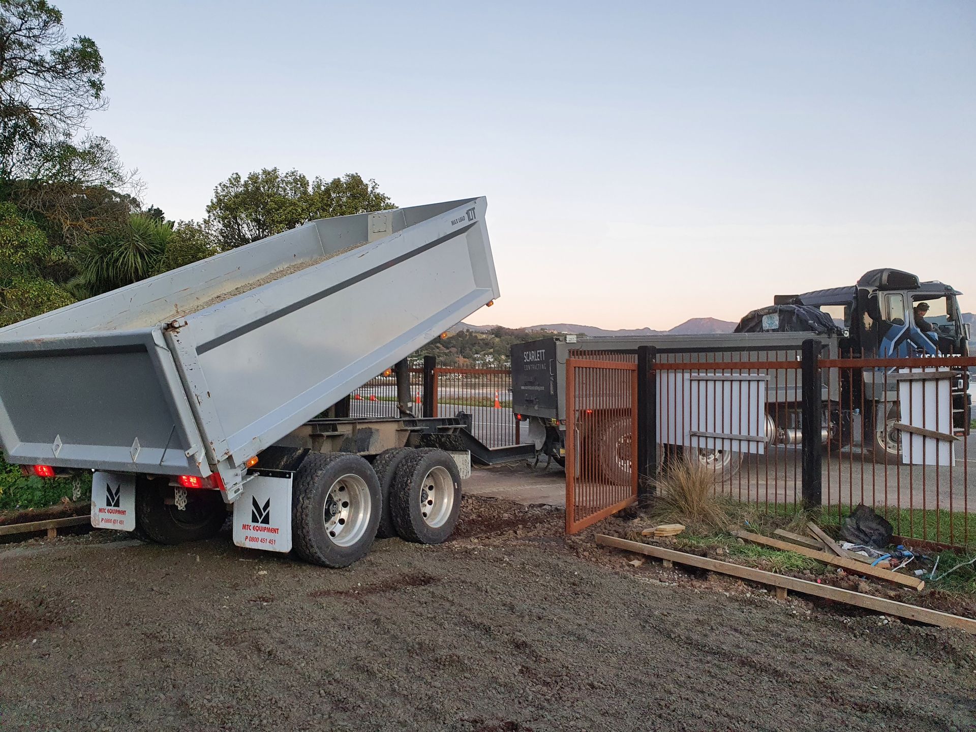 A dump truck is parked in a gravel lot next to a fence.
