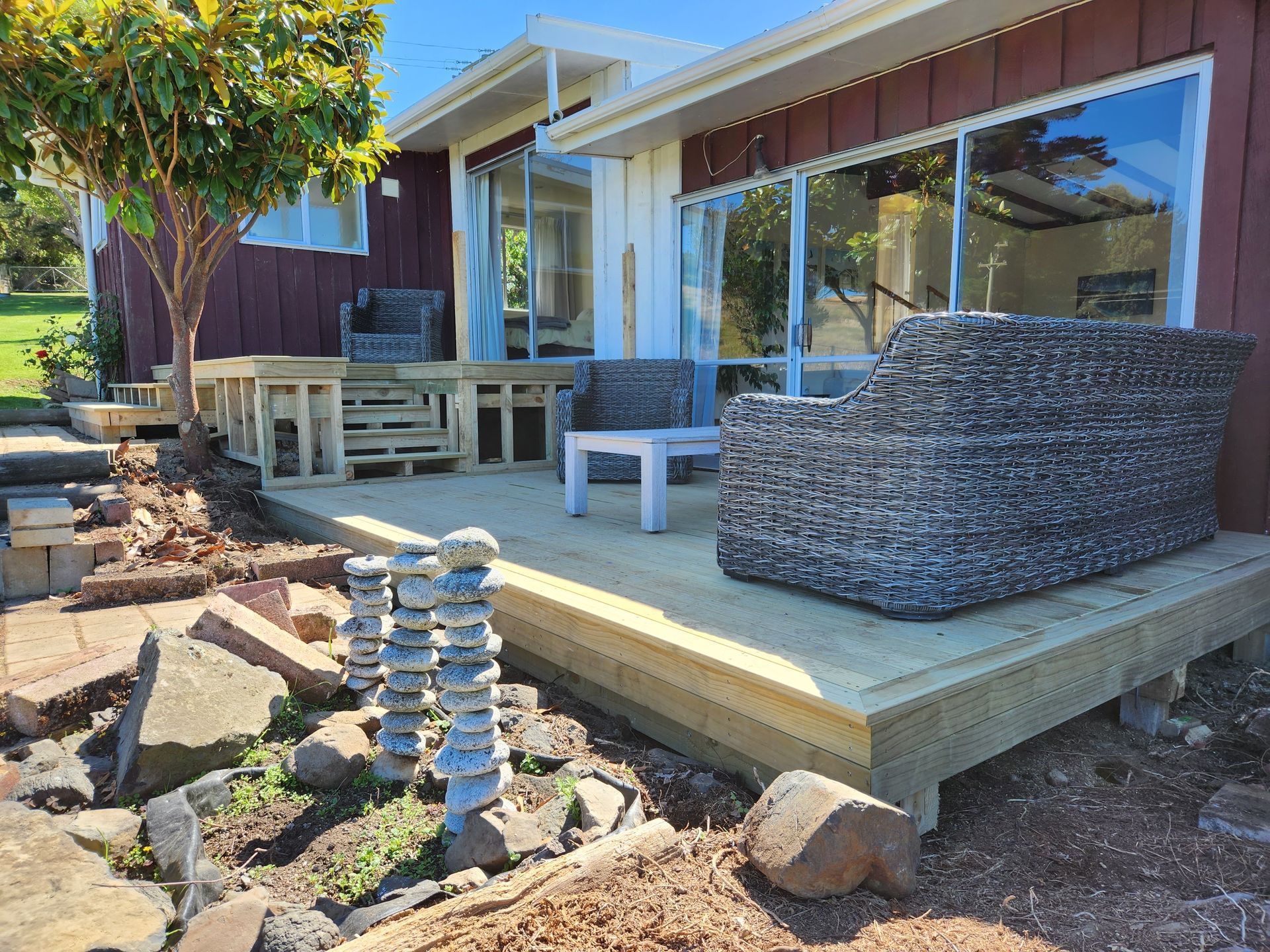 A wooden deck with a couch and chairs in front of a house.