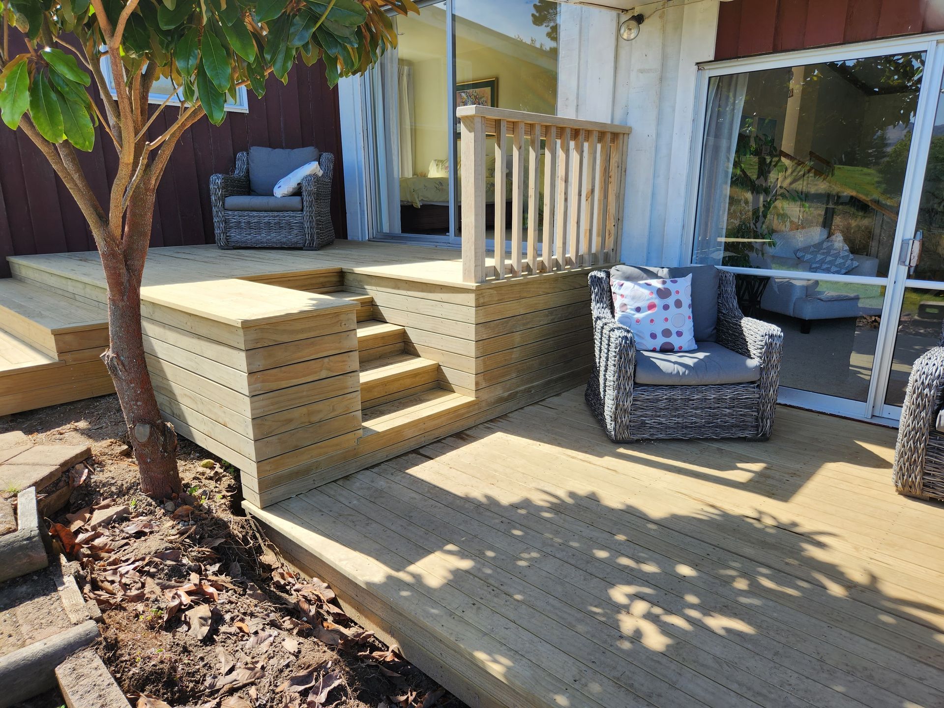A wooden deck with chairs and a tree in front of a house.