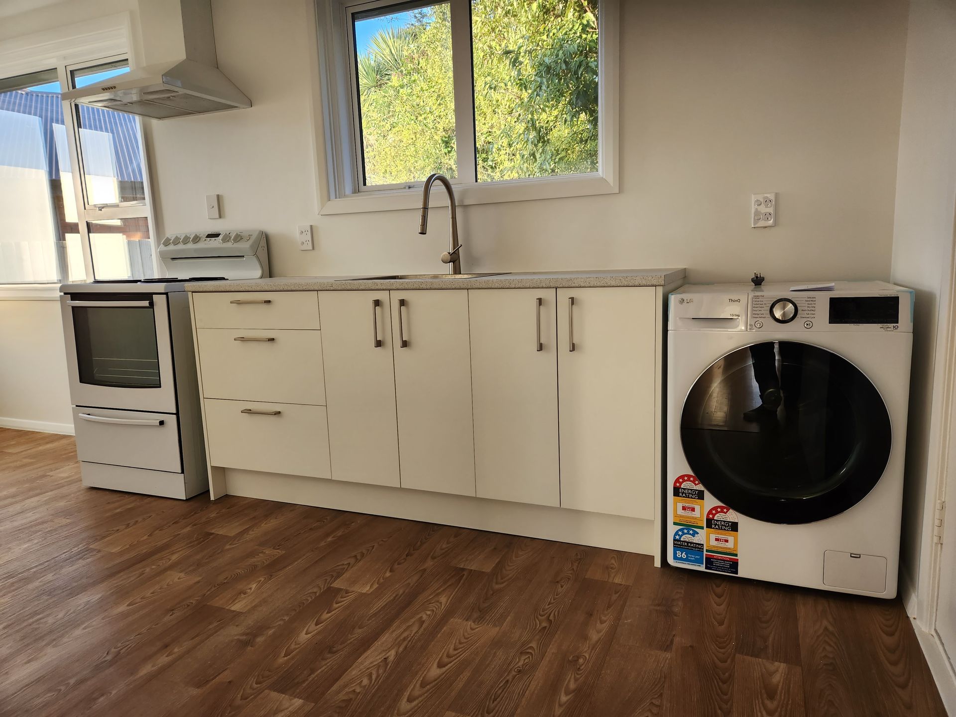 A kitchen with white cabinets , a washer and dryer , and a window.