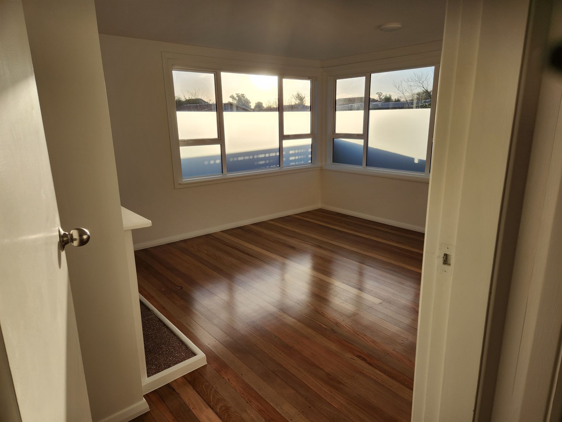 An empty room with hardwood floors and lots of windows.