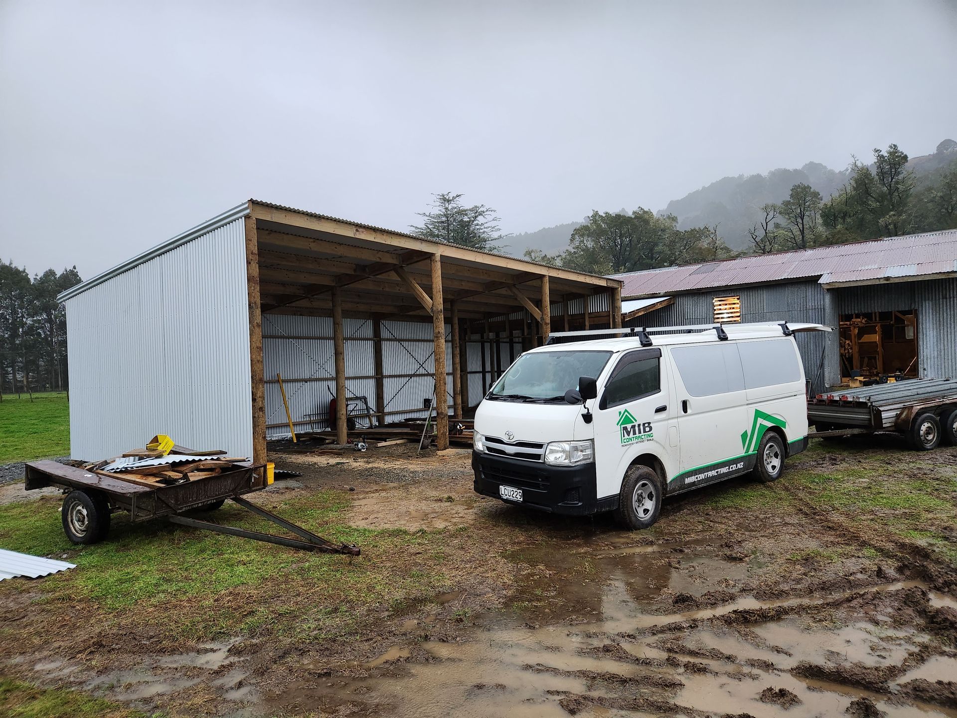 A white van is parked in a muddy field in front of a building.