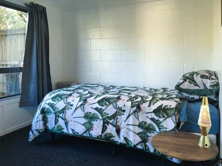 A bedroom with a bed , nightstand , lamp and window.