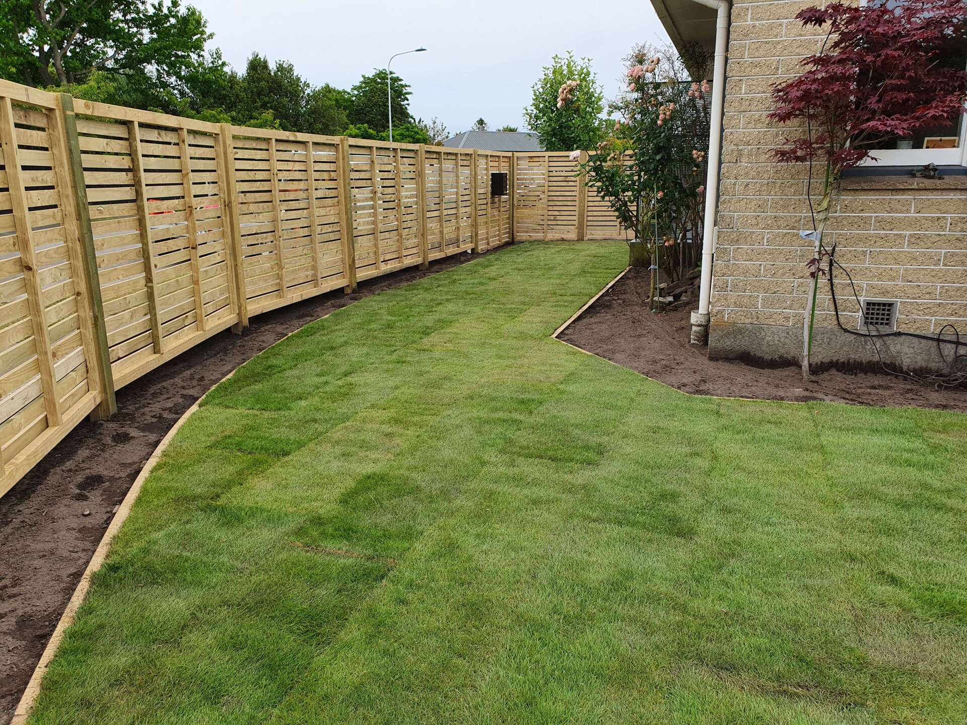A wooden fence surrounds a lush green lawn in a backyard.