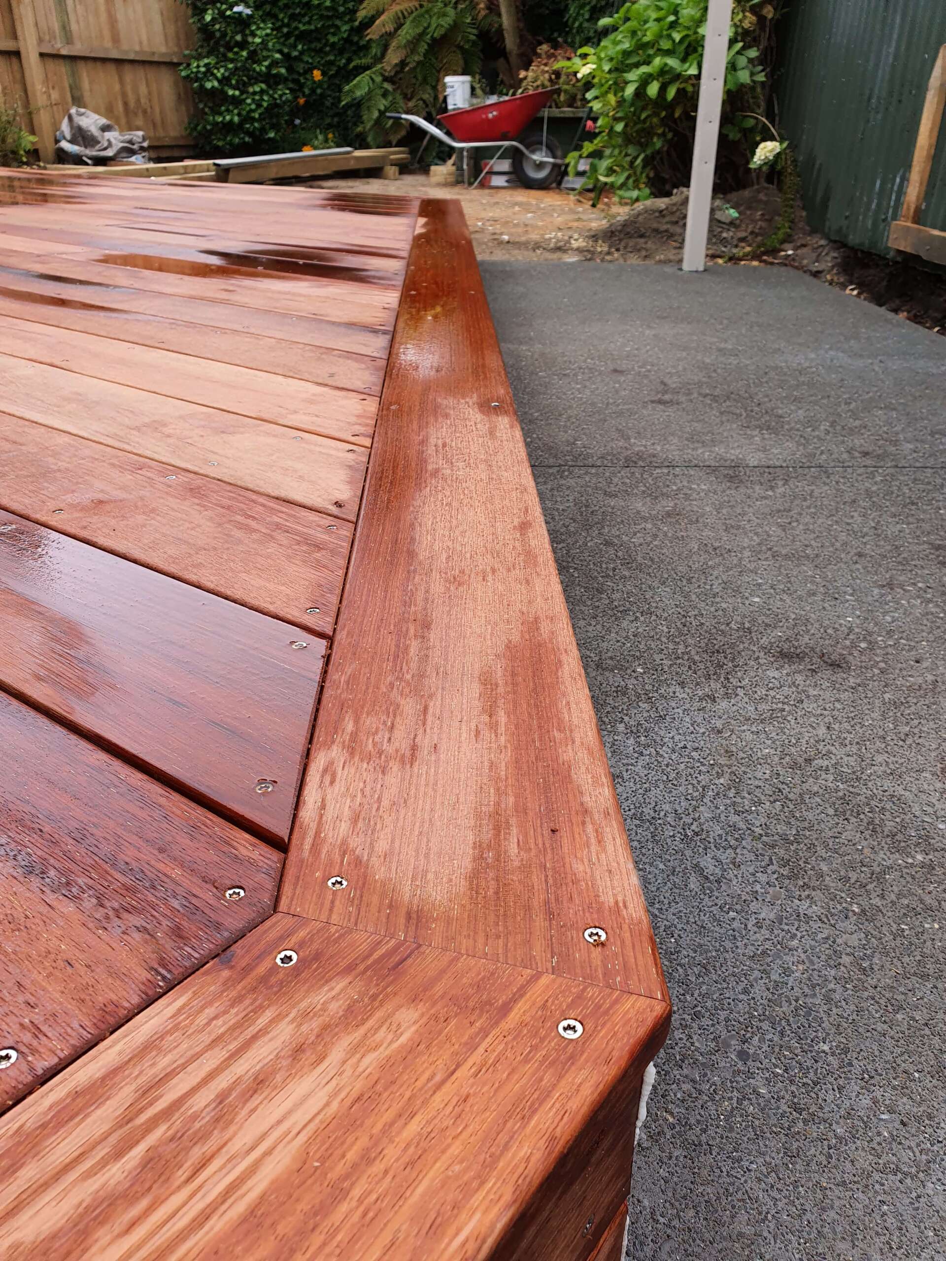 A close up of a wooden deck with a wheelbarrow in the background.
