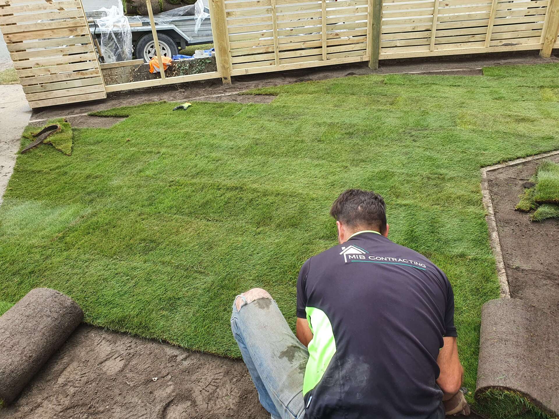 A man is kneeling down in front of a lush green lawn.