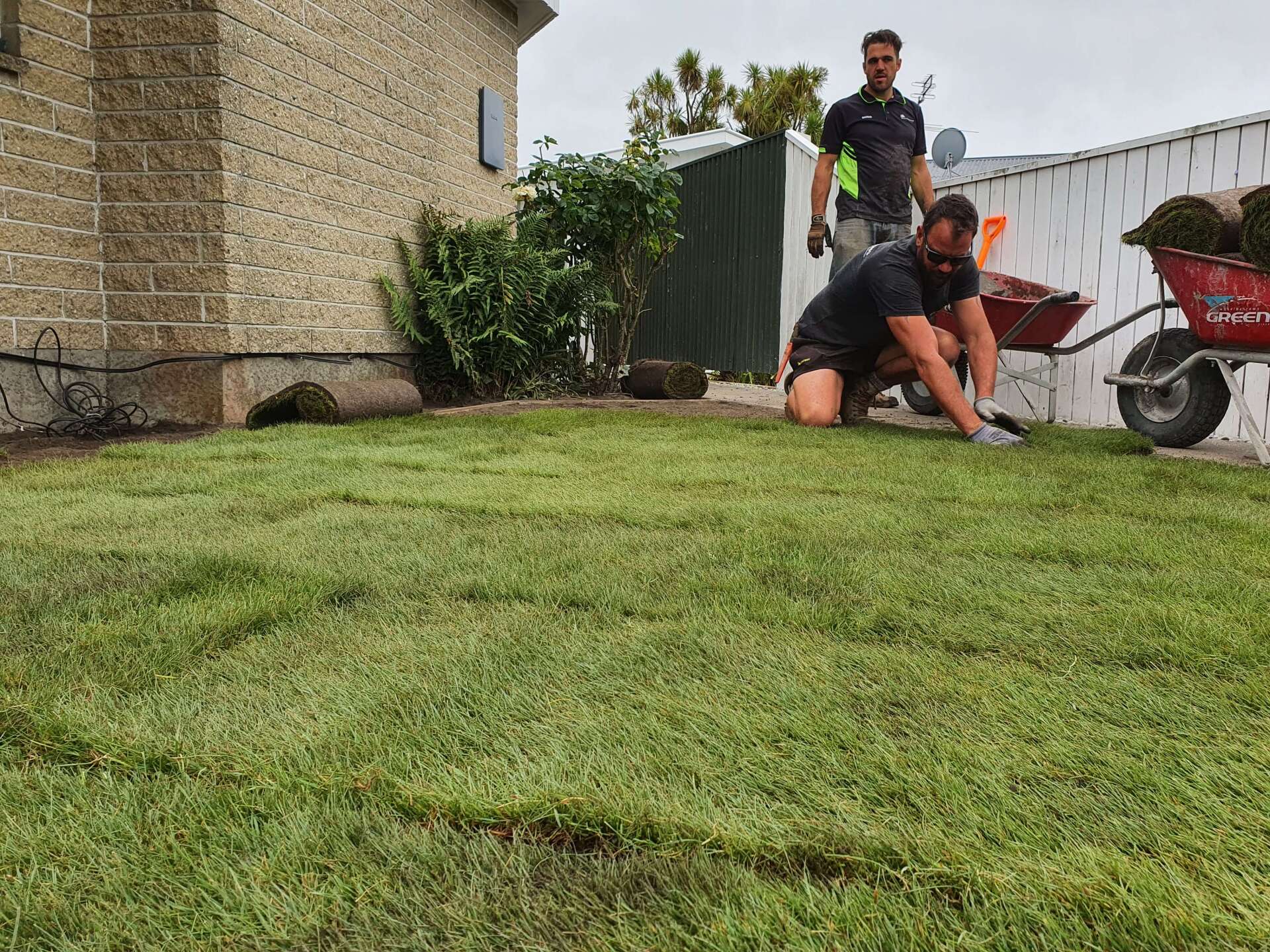 Two men are working on a lush green lawn in front of a house.
