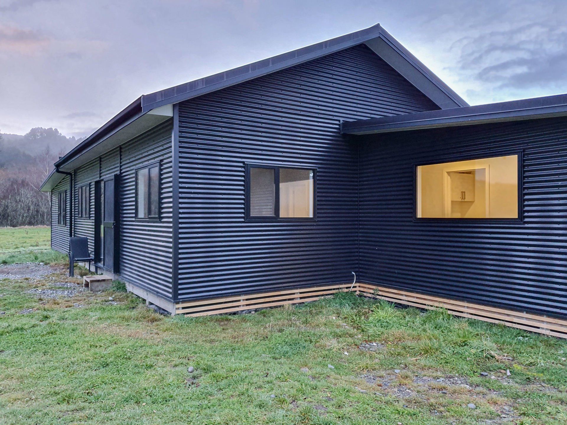 A black house with a yellow window is sitting in the middle of a grassy field.
