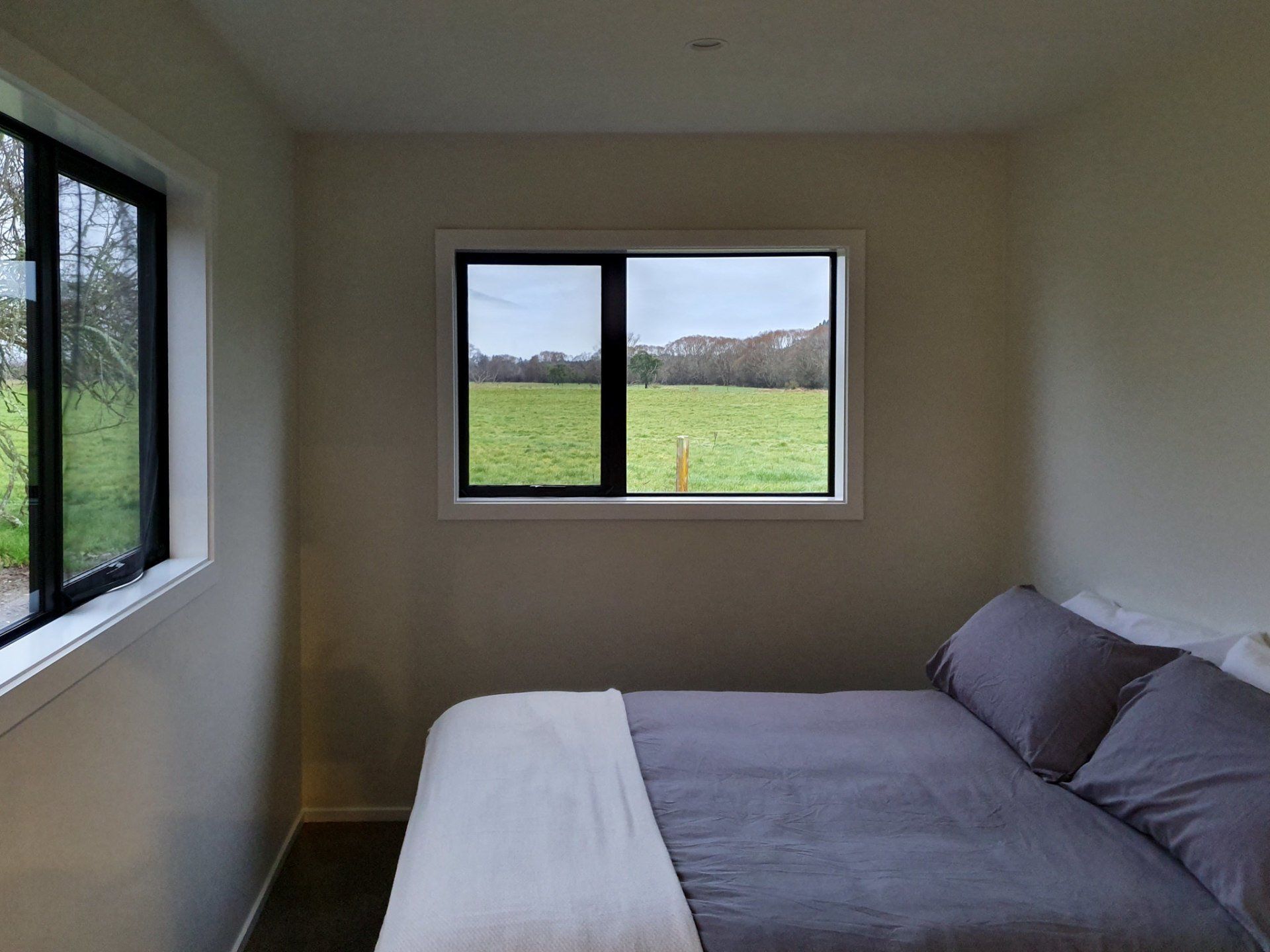 A bedroom with a bed and a window with a field in the background