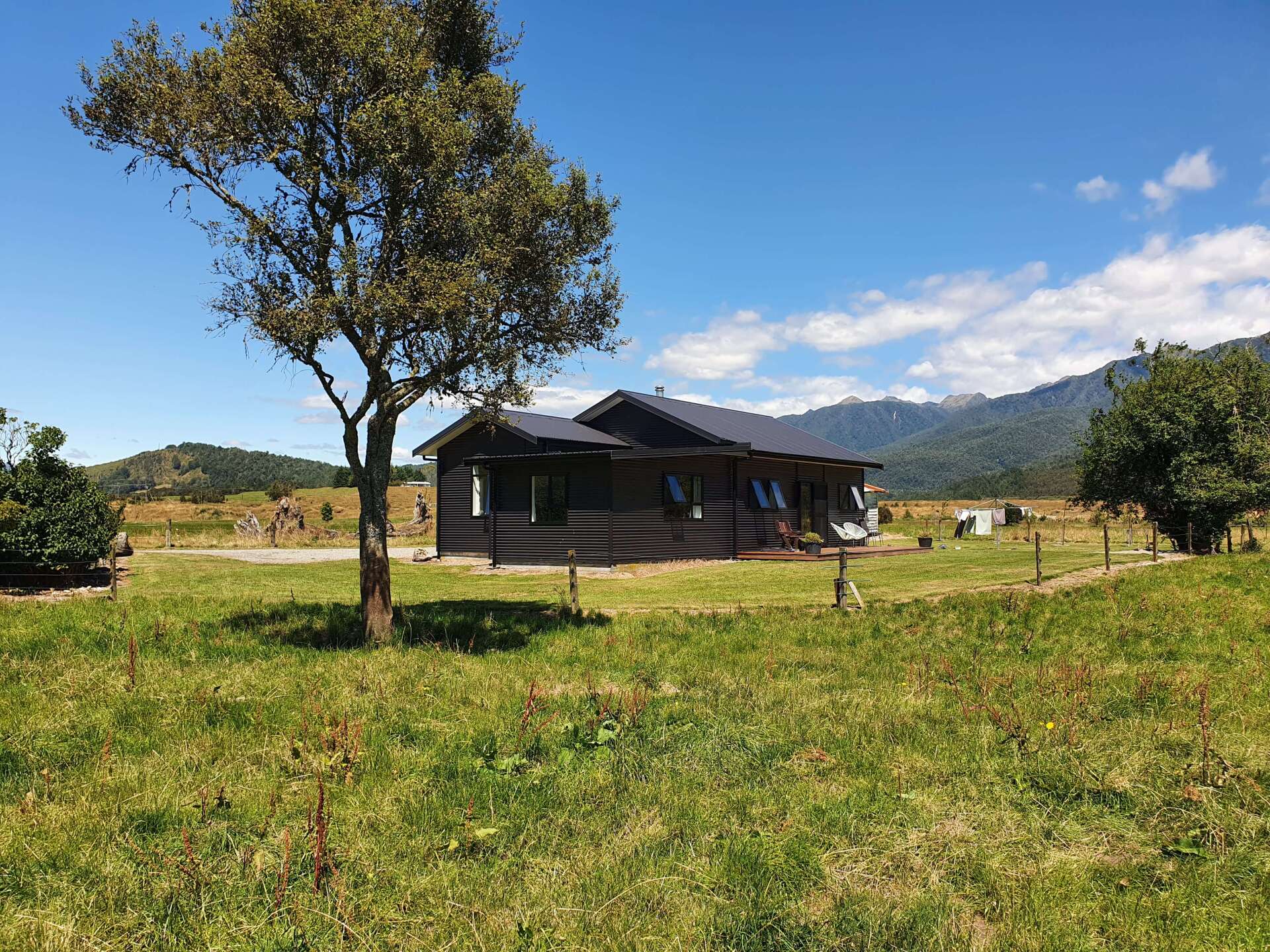 A house is sitting in the middle of a grassy field with mountains in the background.