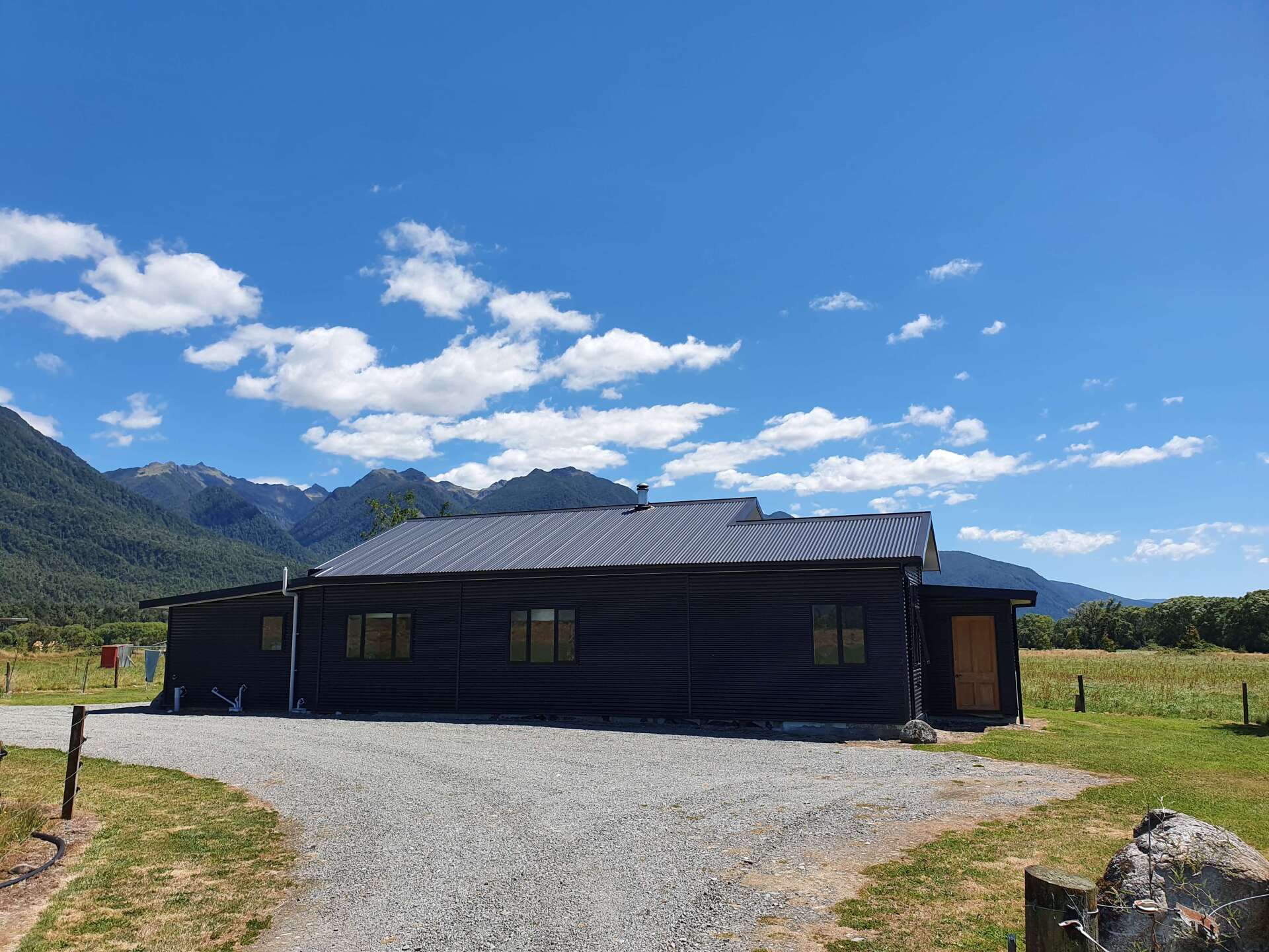 A log cabin is sitting in the middle of a grassy field with mountains in the background.
