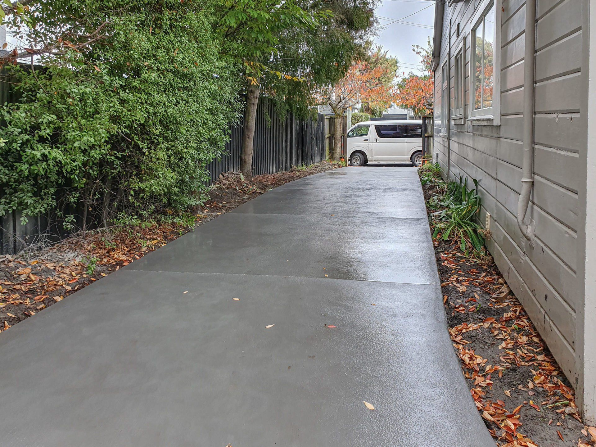 A concrete driveway leading to a house with a white van parked on the side of it.