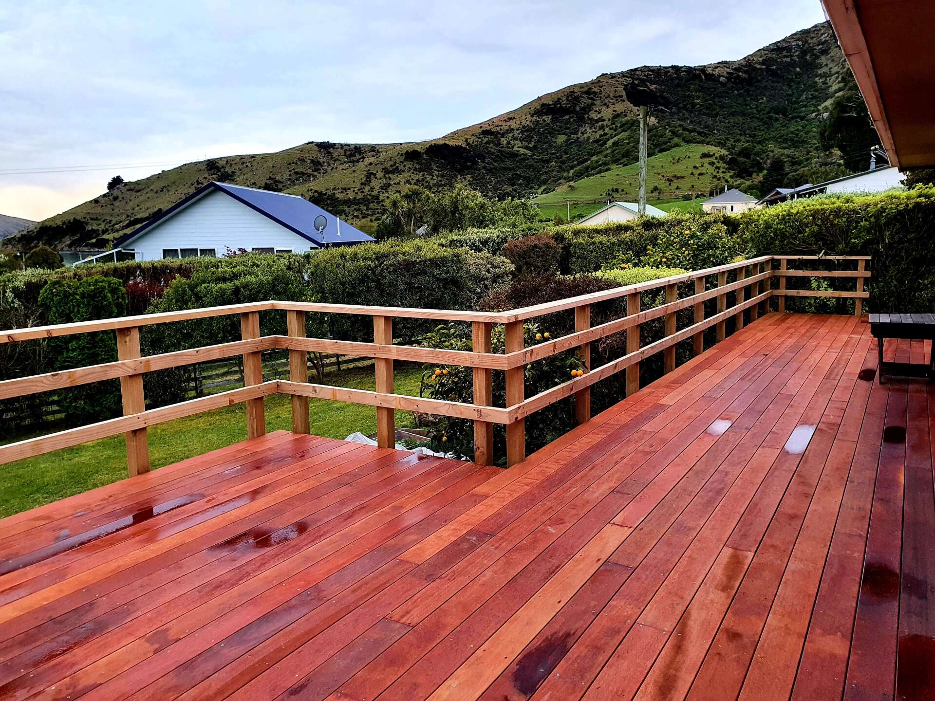 A wooden deck with a wooden railing and a house in the background