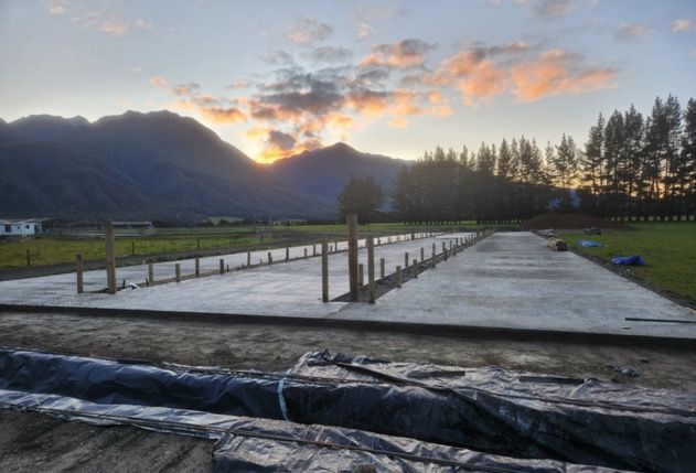 A concrete foundation is being built in a field with mountains in the background at sunset.