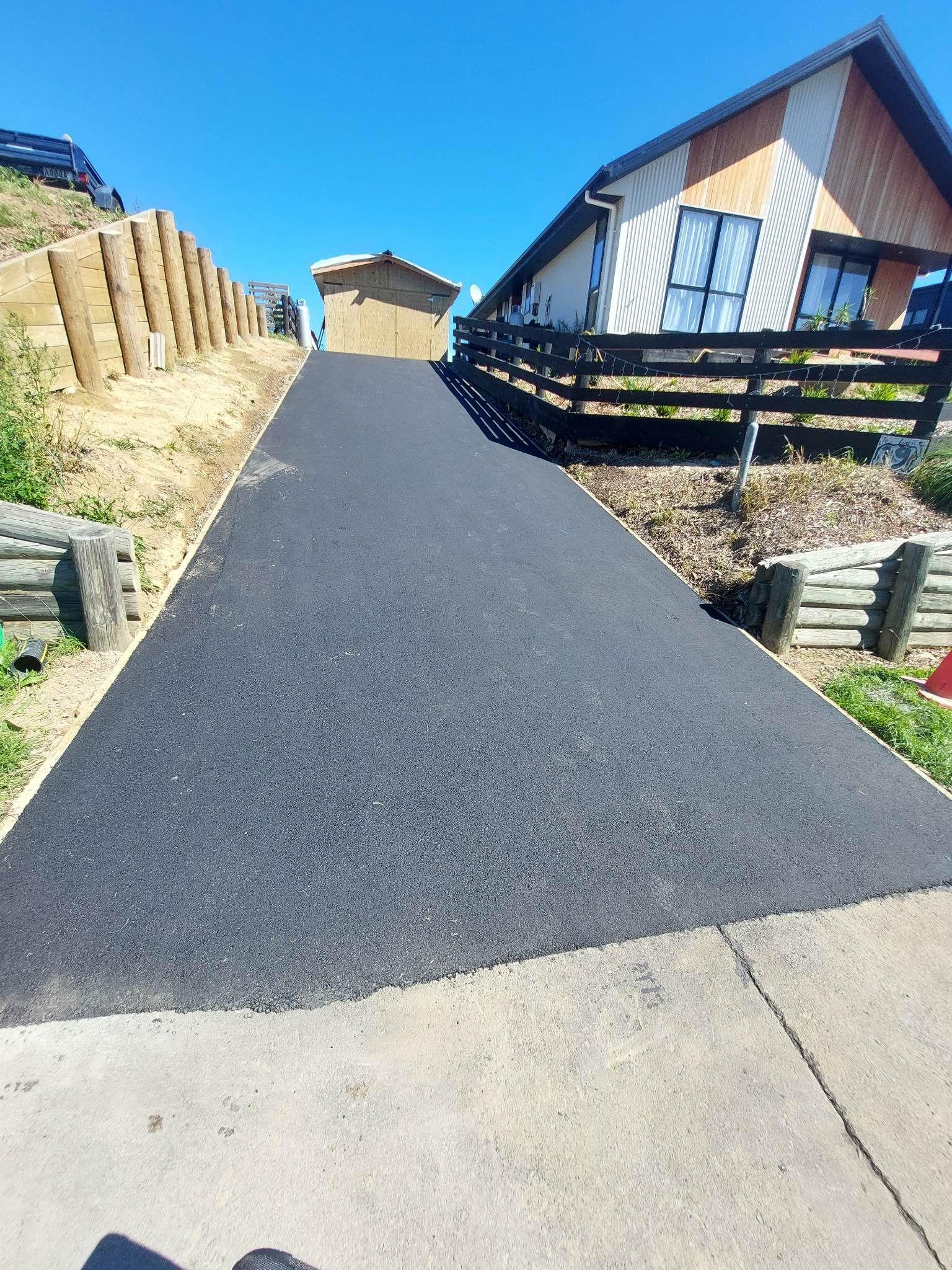 A asphalt driveway leading to a house with a wooden fence.